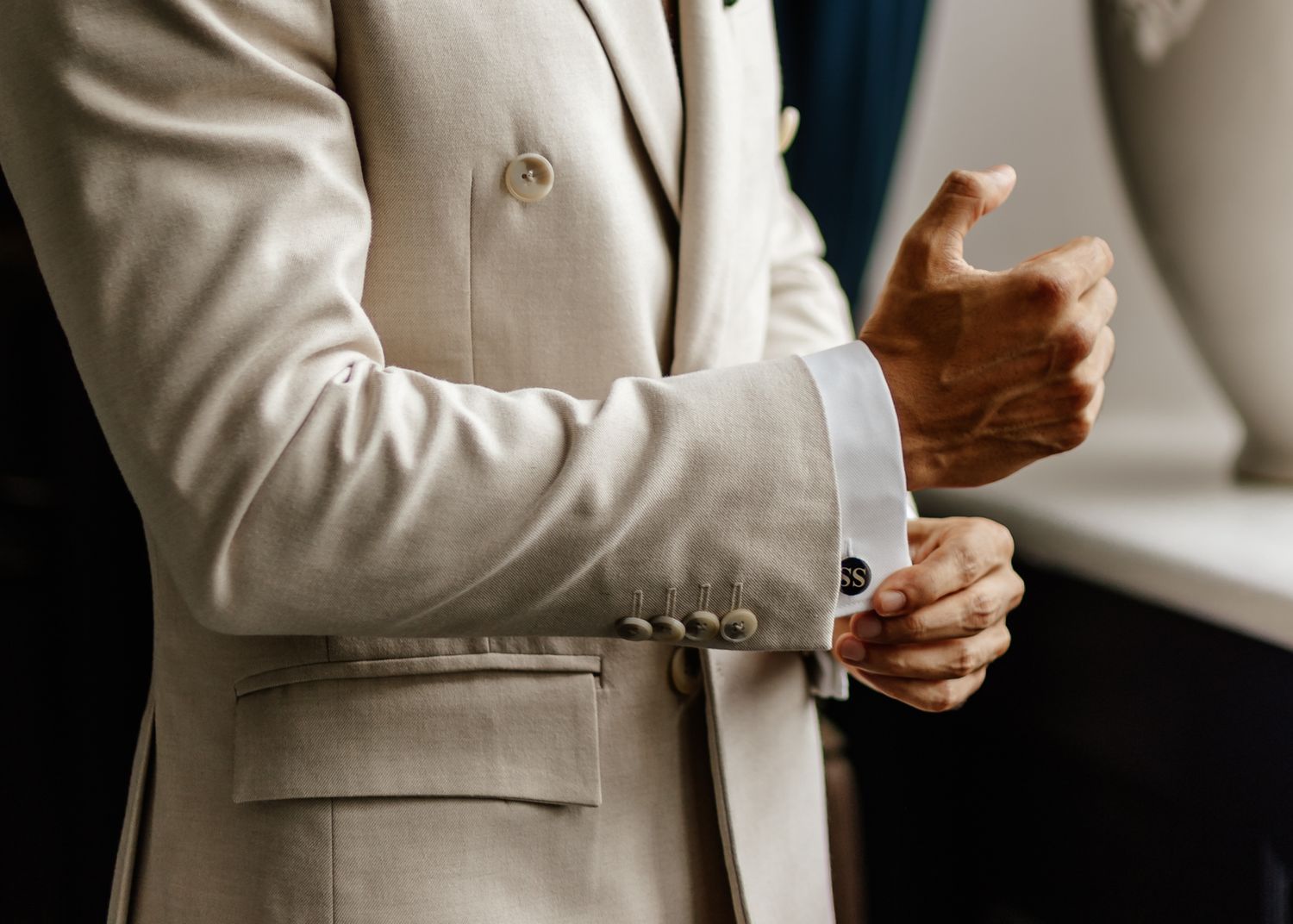 Close-up view of hands adjusting a light beige suit jacket sleeve and cuff in natural lighting.