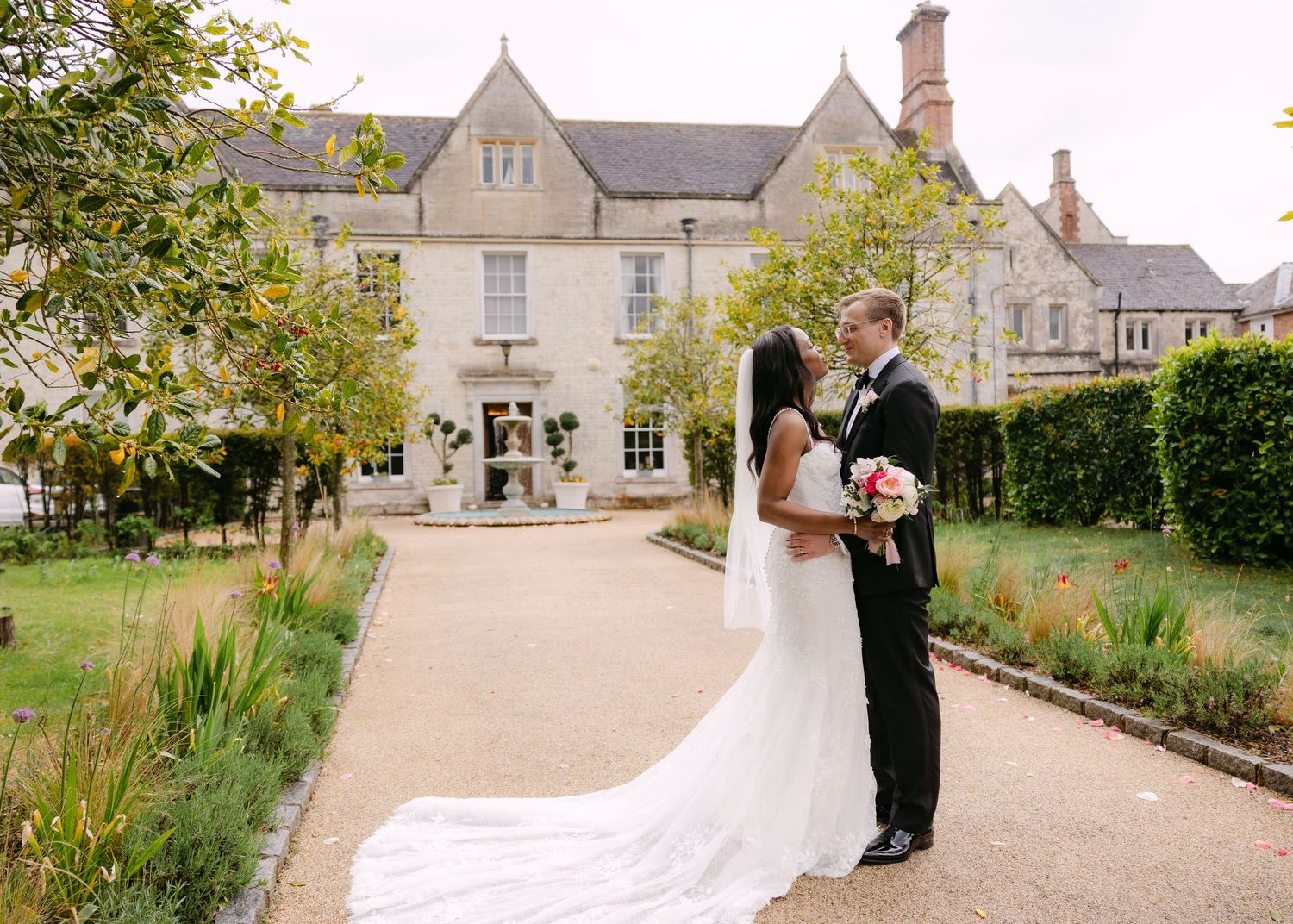 Bride and groom share a romantic moment in front of an elegant English manor house on their wedding day.