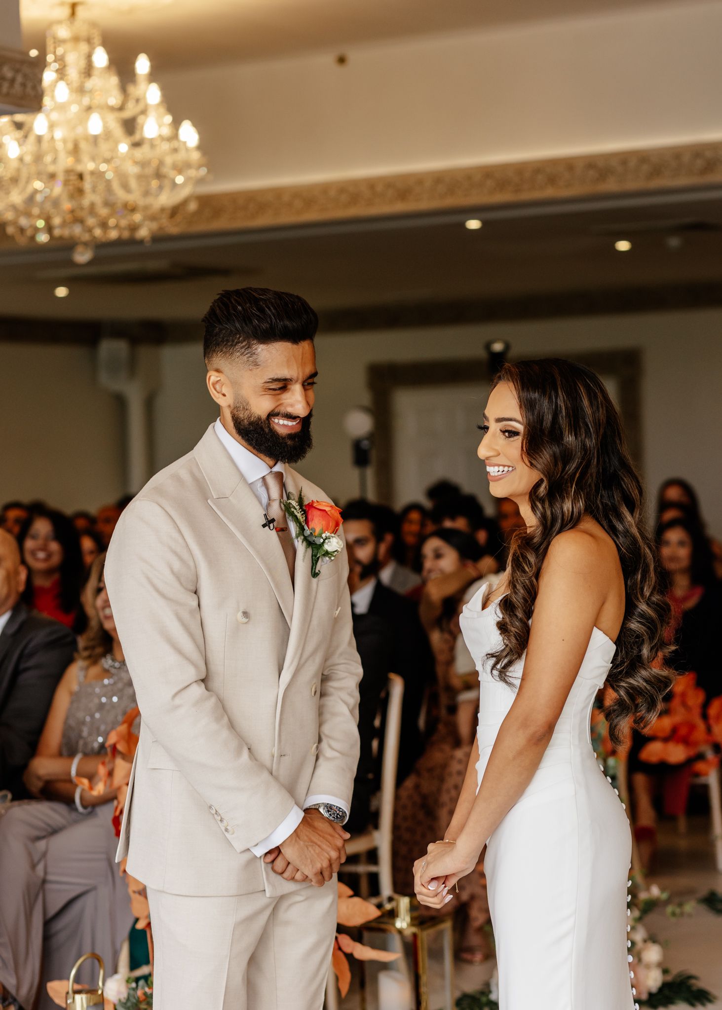 A couple shares a joyful moment during their wedding ceremony under an elegant crystal chandelier in a formal venue.