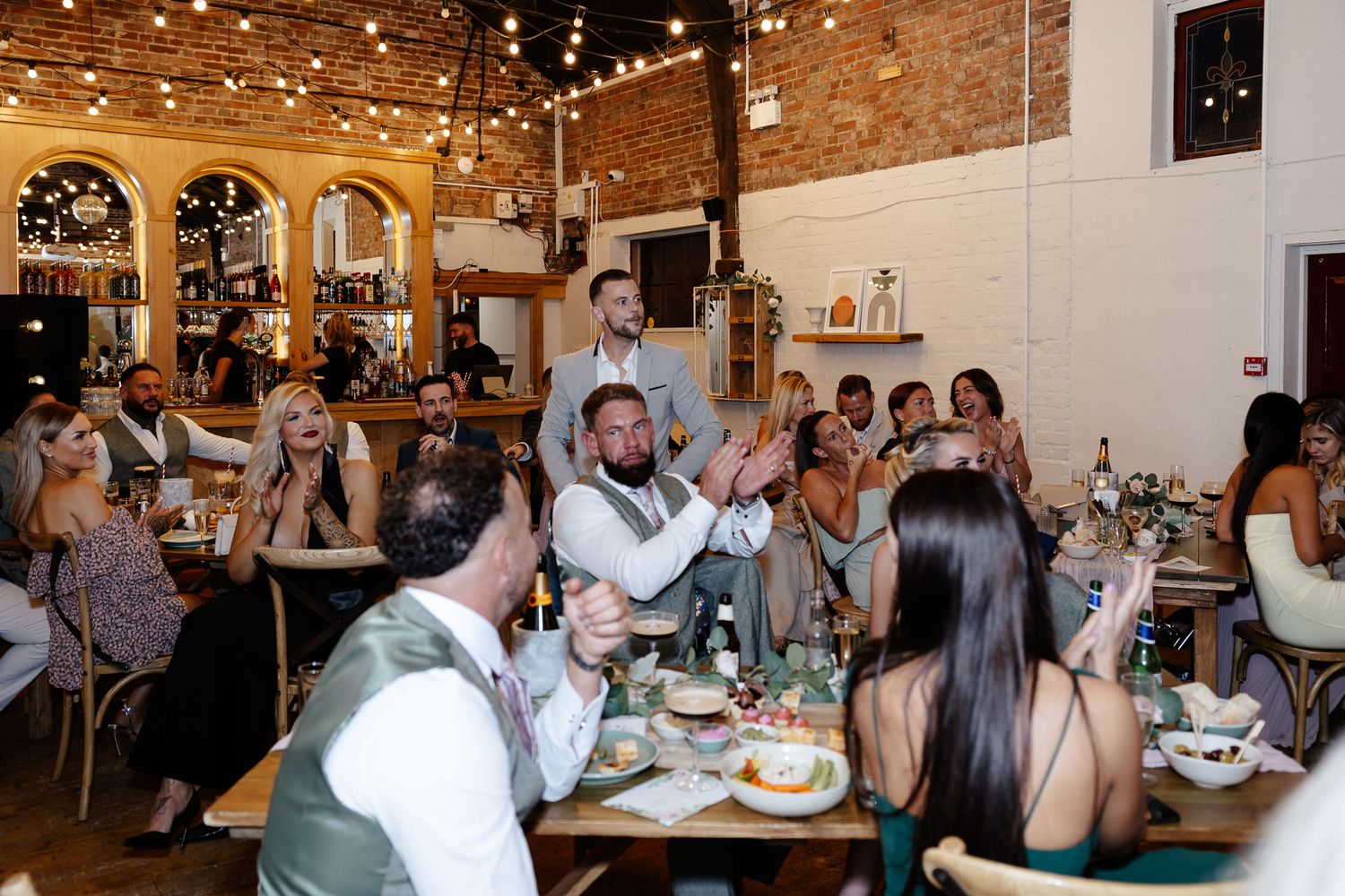 Panoramic view of wedding reception dinner with guests seated at long tables under warm lighting.