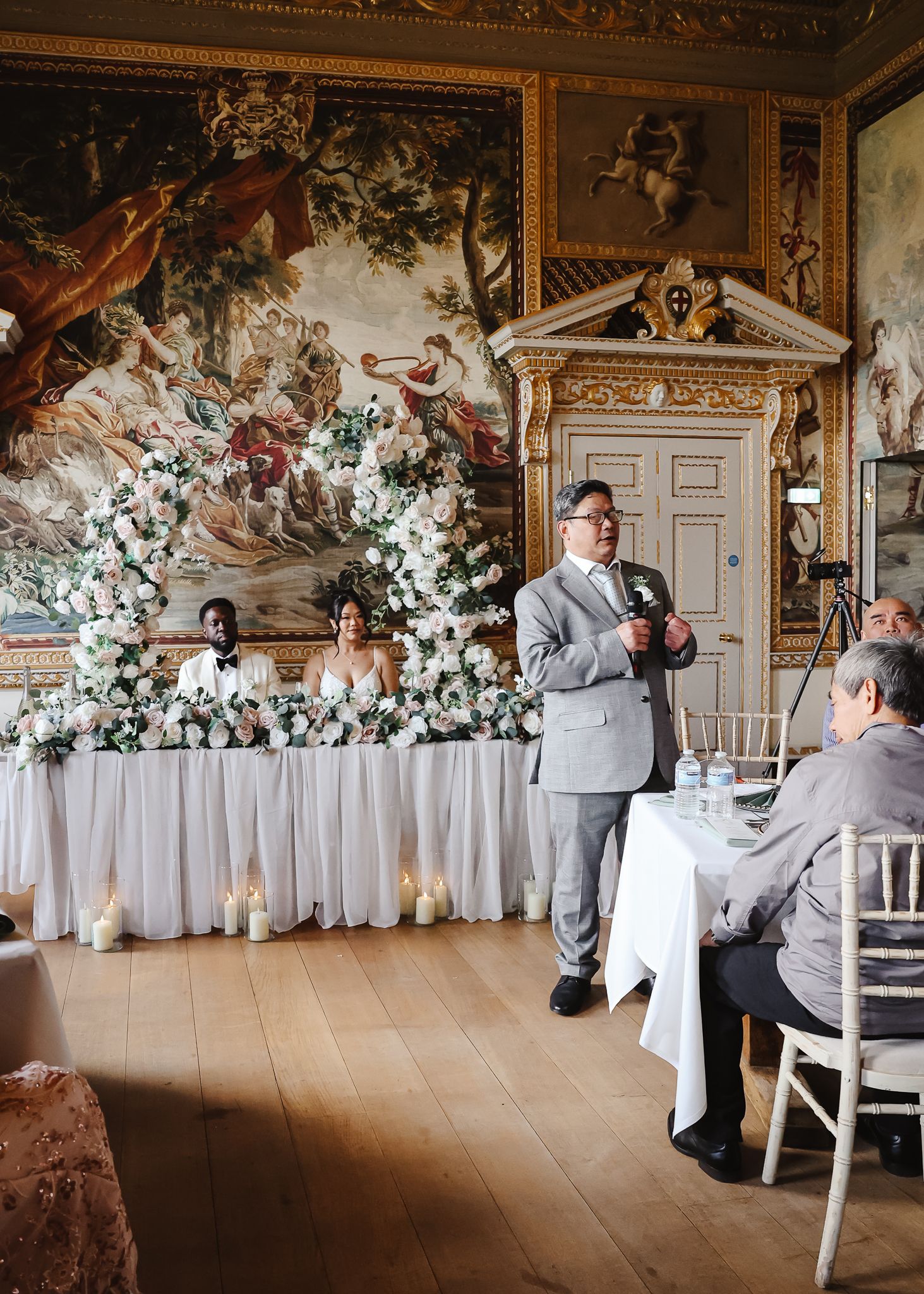 Wedding celebration in ornate room with painted murals and white floral decorations.