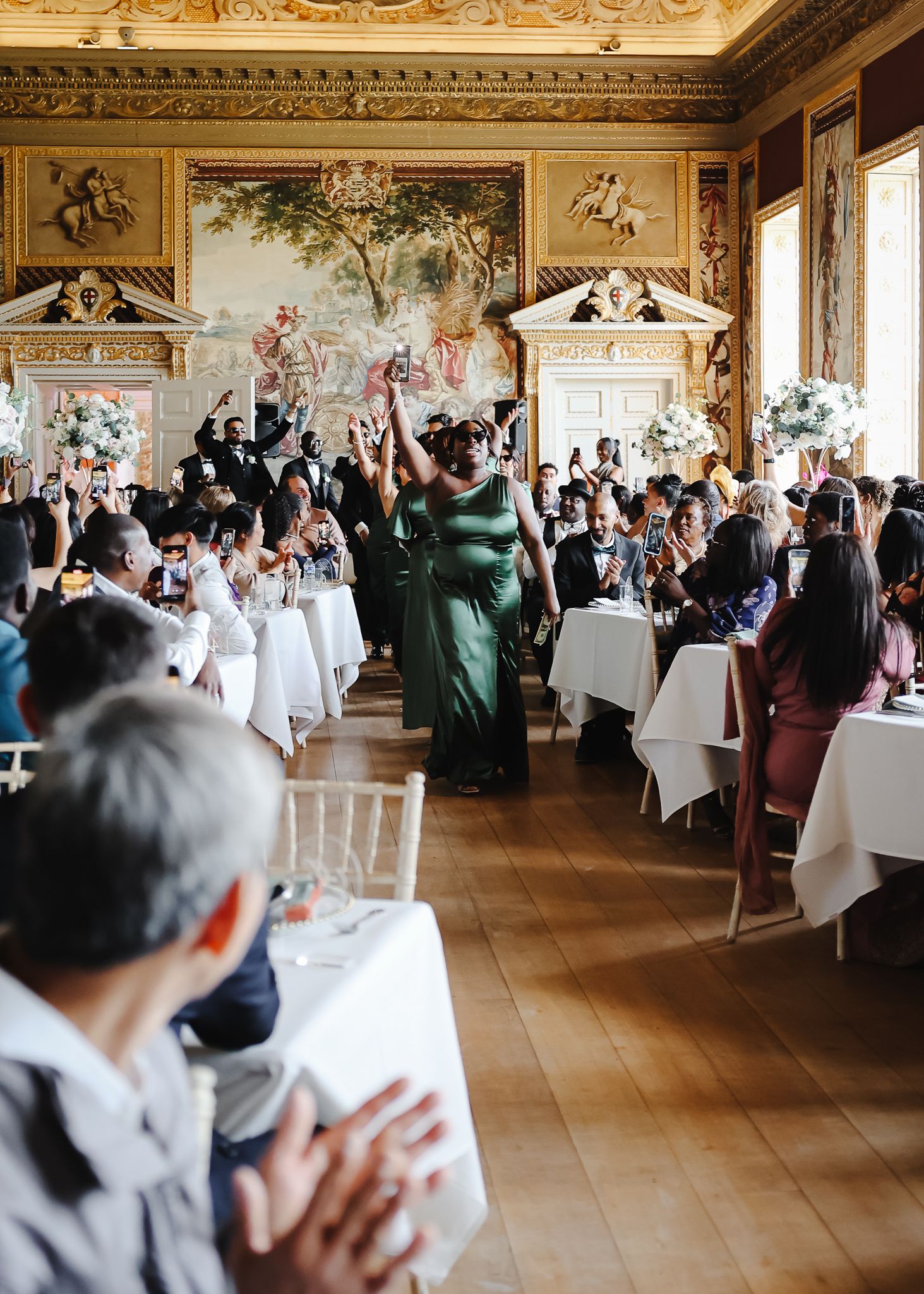 Ornate reception hall with frescoed ceiling and guests seated at white-clothed tables for wedding celebration.