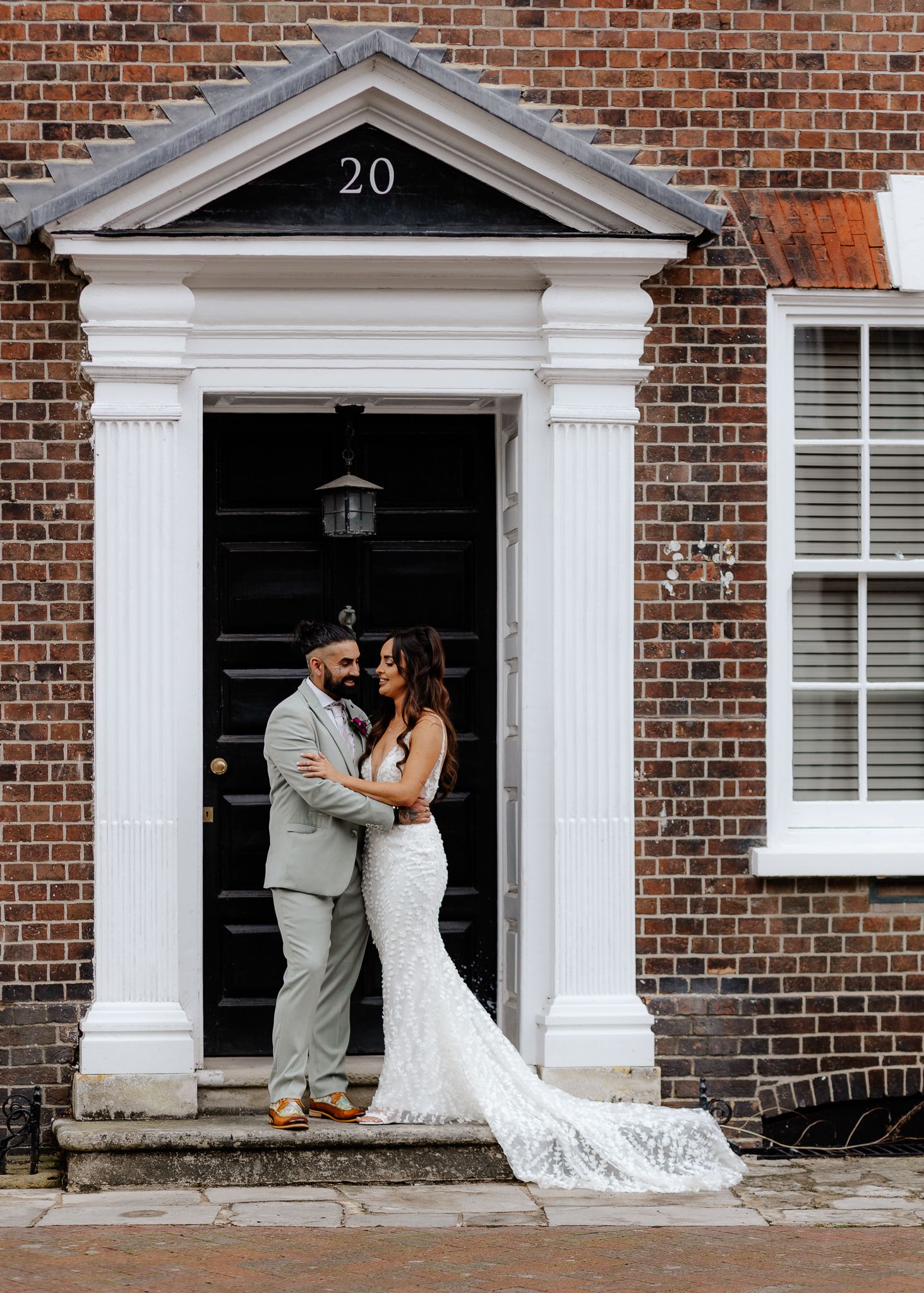 A wedding couple poses in front of a classic red brick building with white columned doorways.