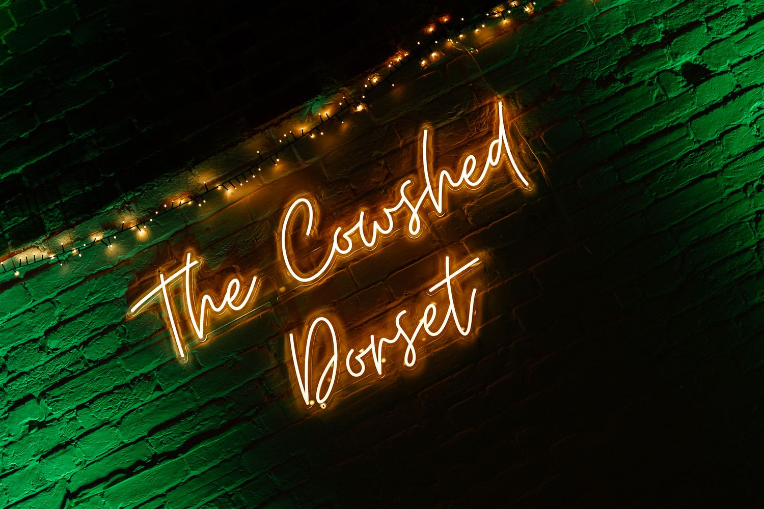 Orange neon sign reading 'The Crushed Posset' glows against a green textured wall with string lights above.