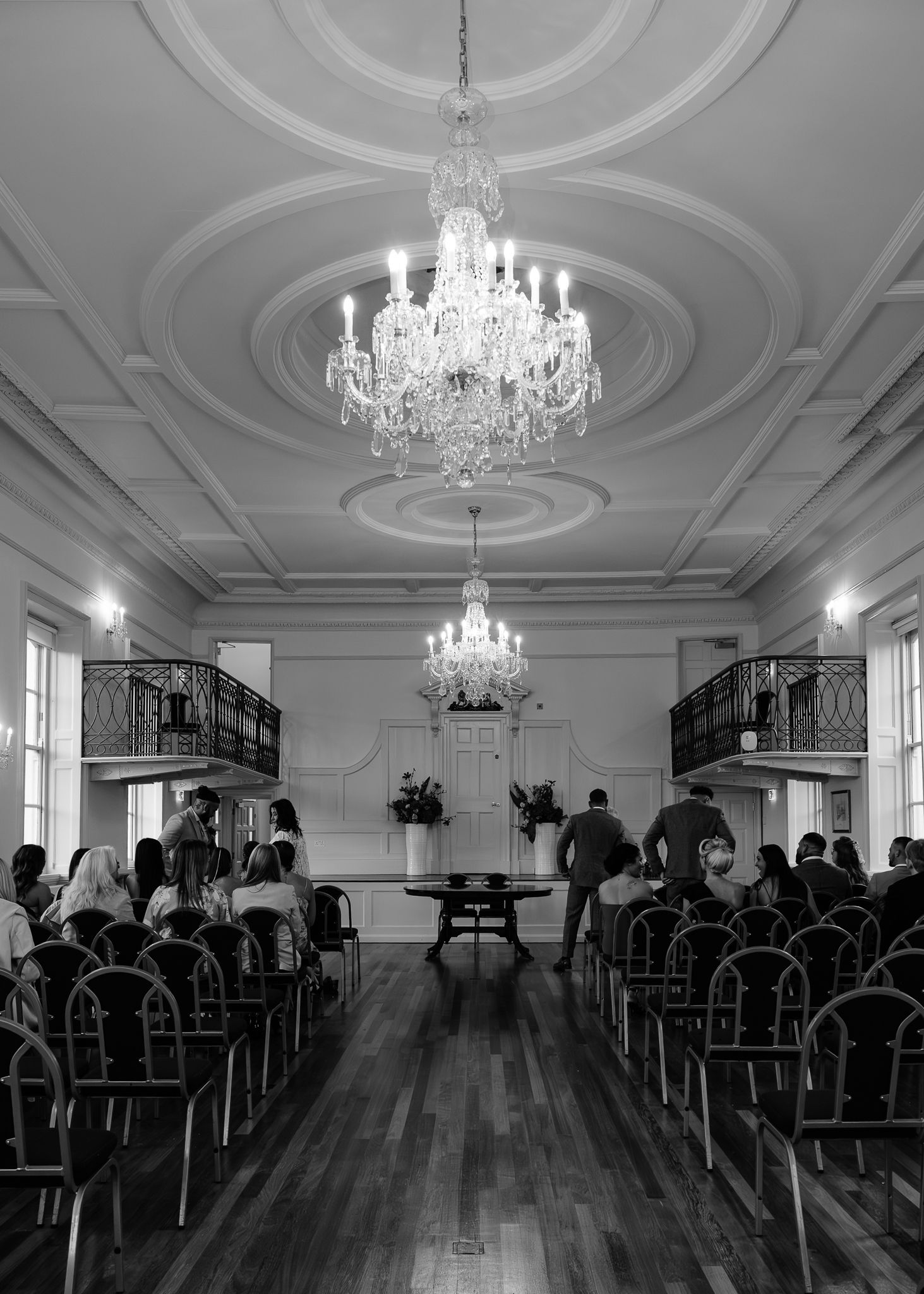 An elegant ballroom with crystal chandeliers and ornate ceiling moldings features a polished hardwood dance floor.