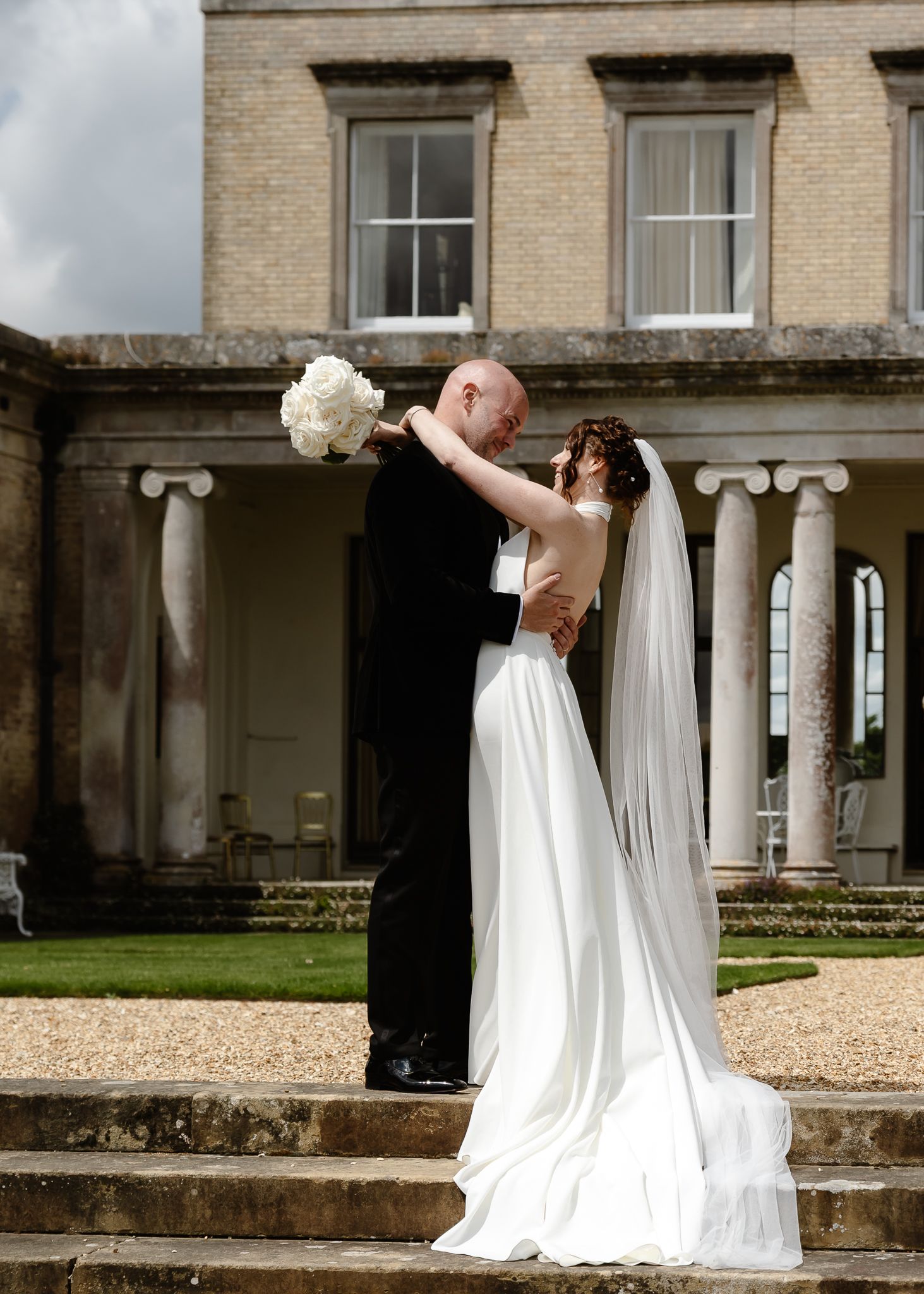 A romantic wedding moment captured on the steps of a grand historic building with classical columns.