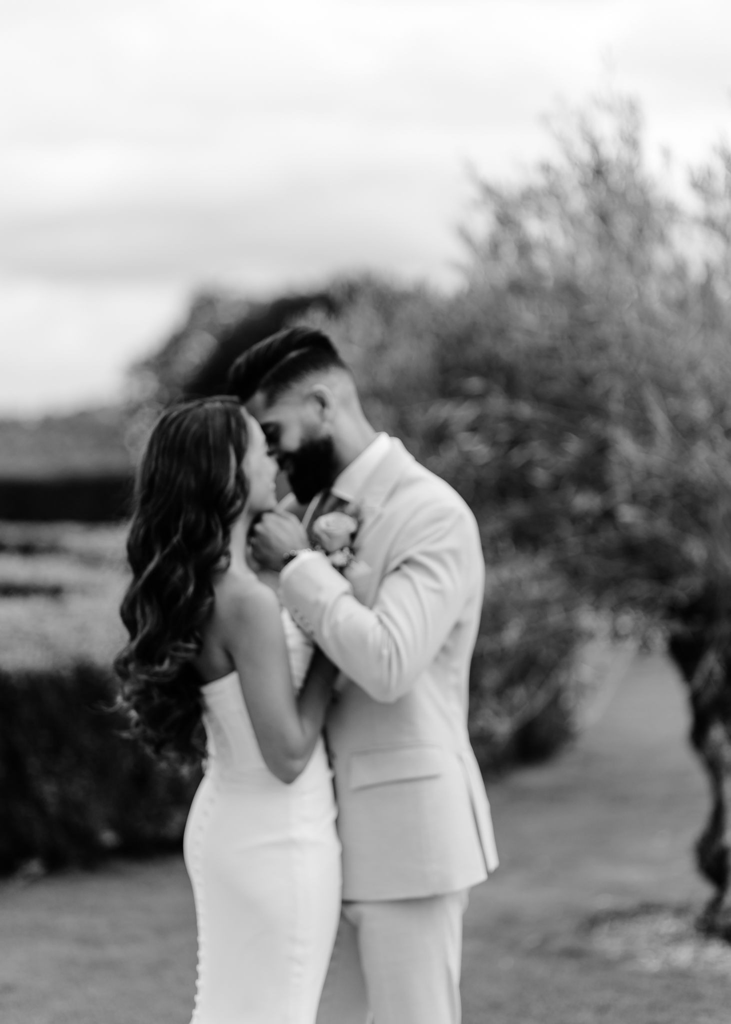 A romantic black and white wedding photo of a couple embracing outdoors in an intimate moment.