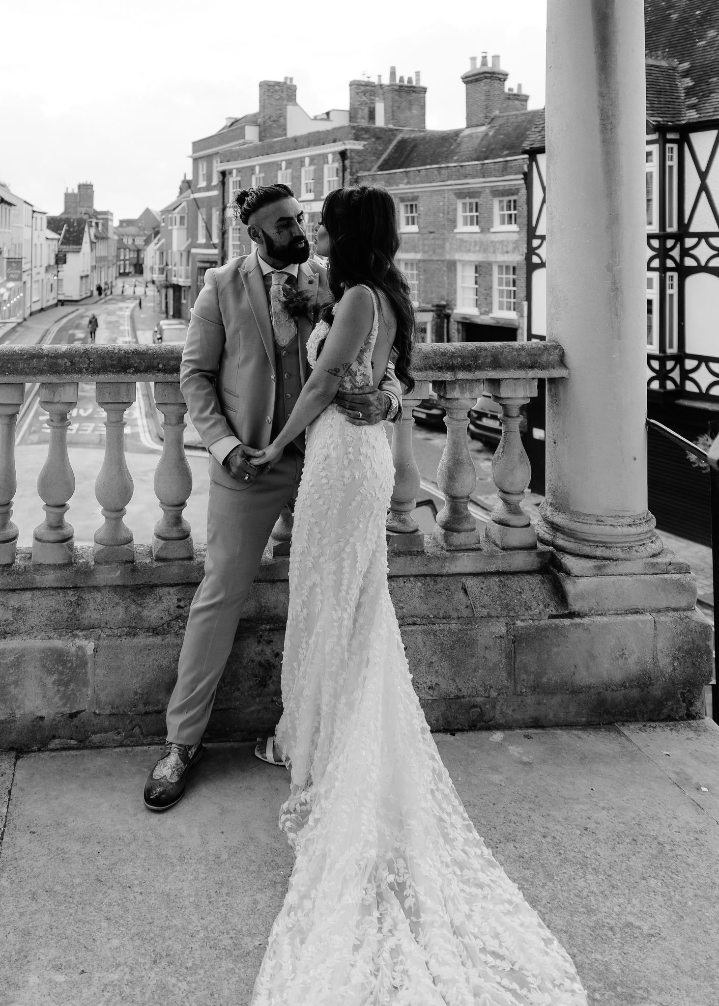 A romantic black and white wedding photo of a couple embracing on a historic balcony with Georgian architecture in background.