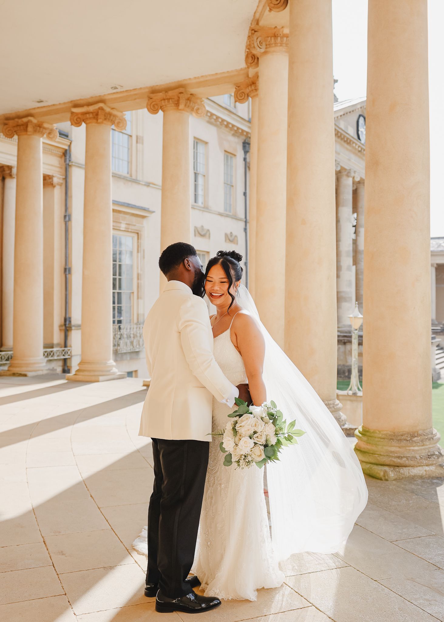 A couple shares romantic dance poses in a sunlit colonnade with classical architecture and white columns.
