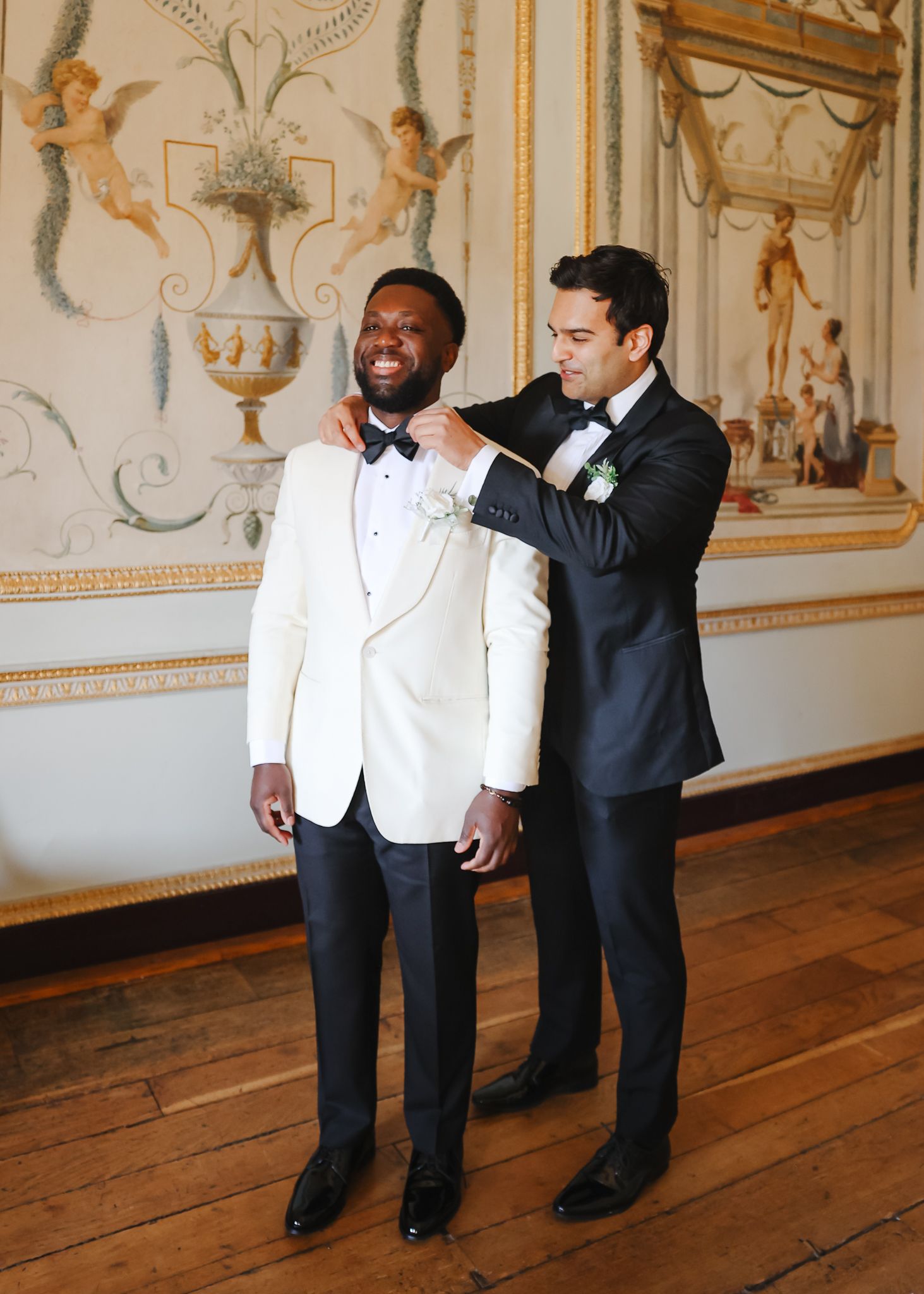 Two people in formal attire share a lighthearted moment in an ornate room with decorative wall panels.