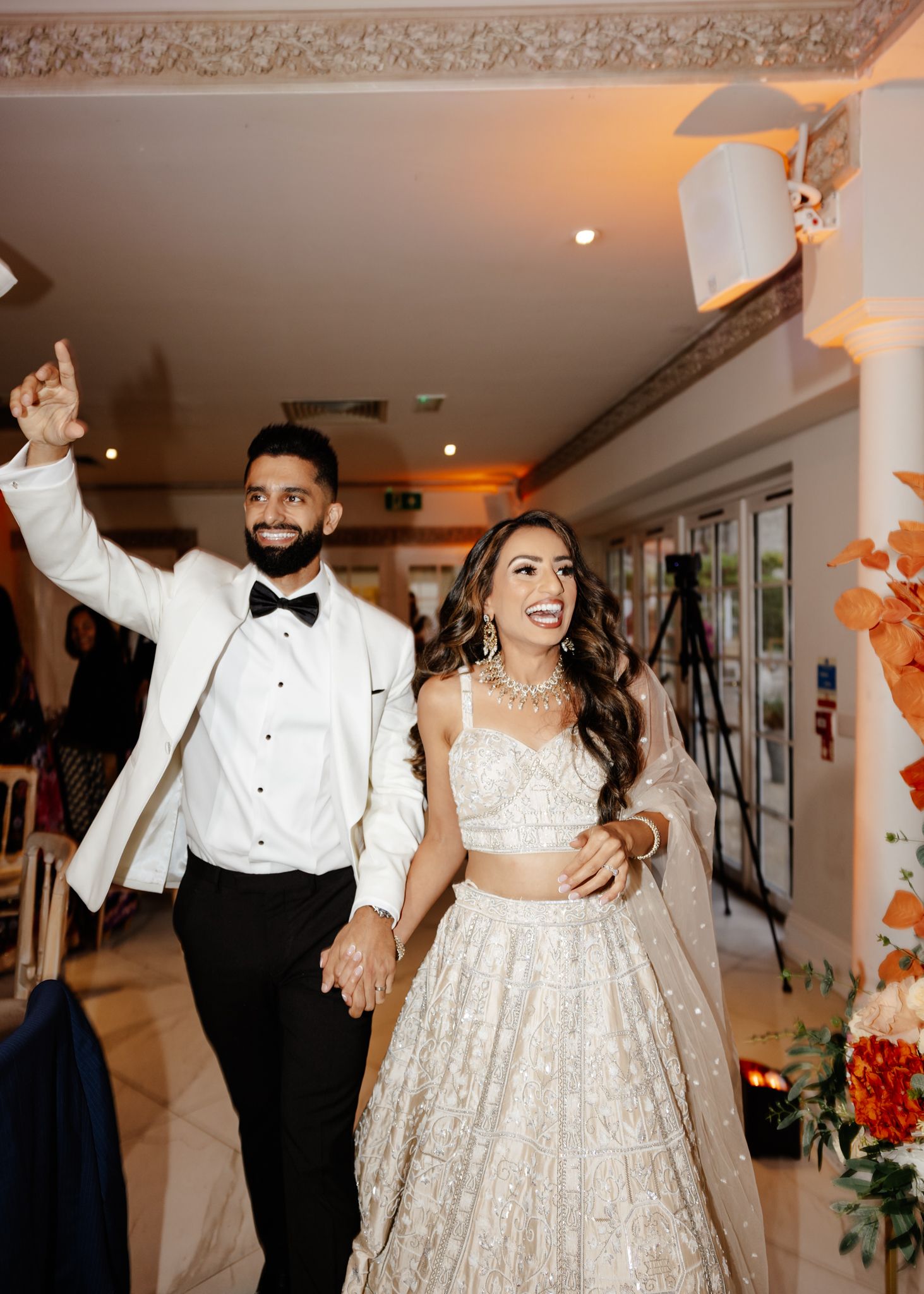 A joyful couple makes their grand entrance at their wedding reception wearing elegant white attire and formal wear.