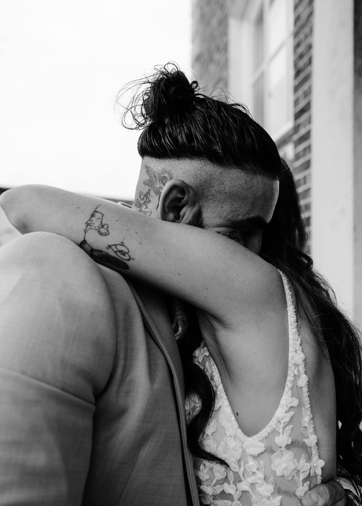A black and white intimate photo showing two people embracing in formal wedding attire.