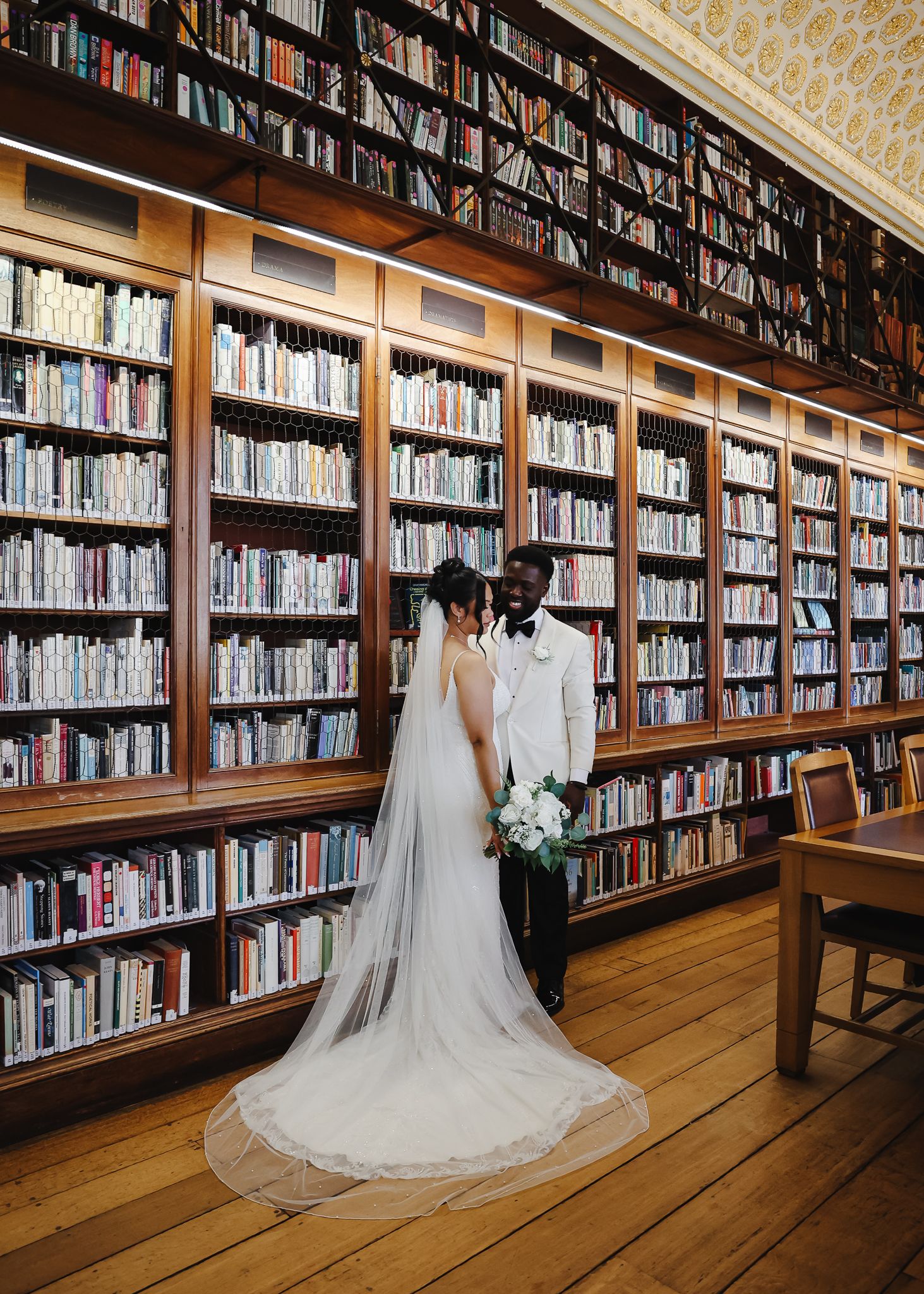 A wedding dress displayed in a grand library with tall wooden bookshelves filled with books creating a romantic backdrop.