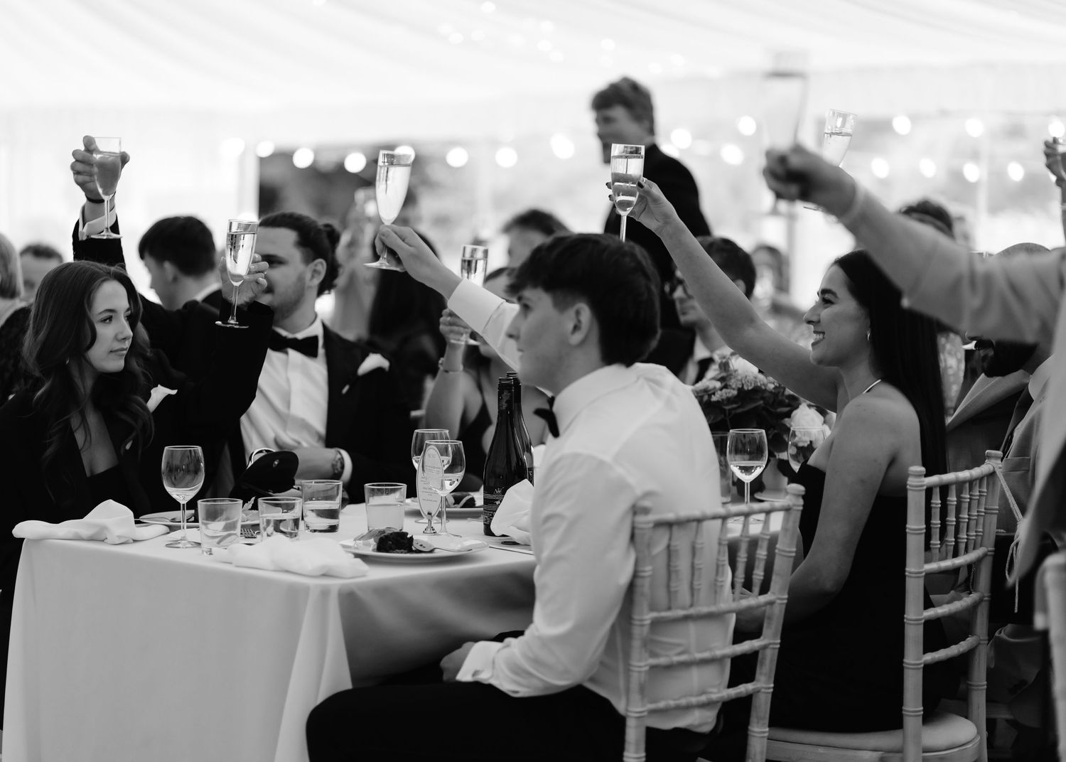 Wedding guests raising champagne glasses in a toast at an elegant reception under a marquee tent.