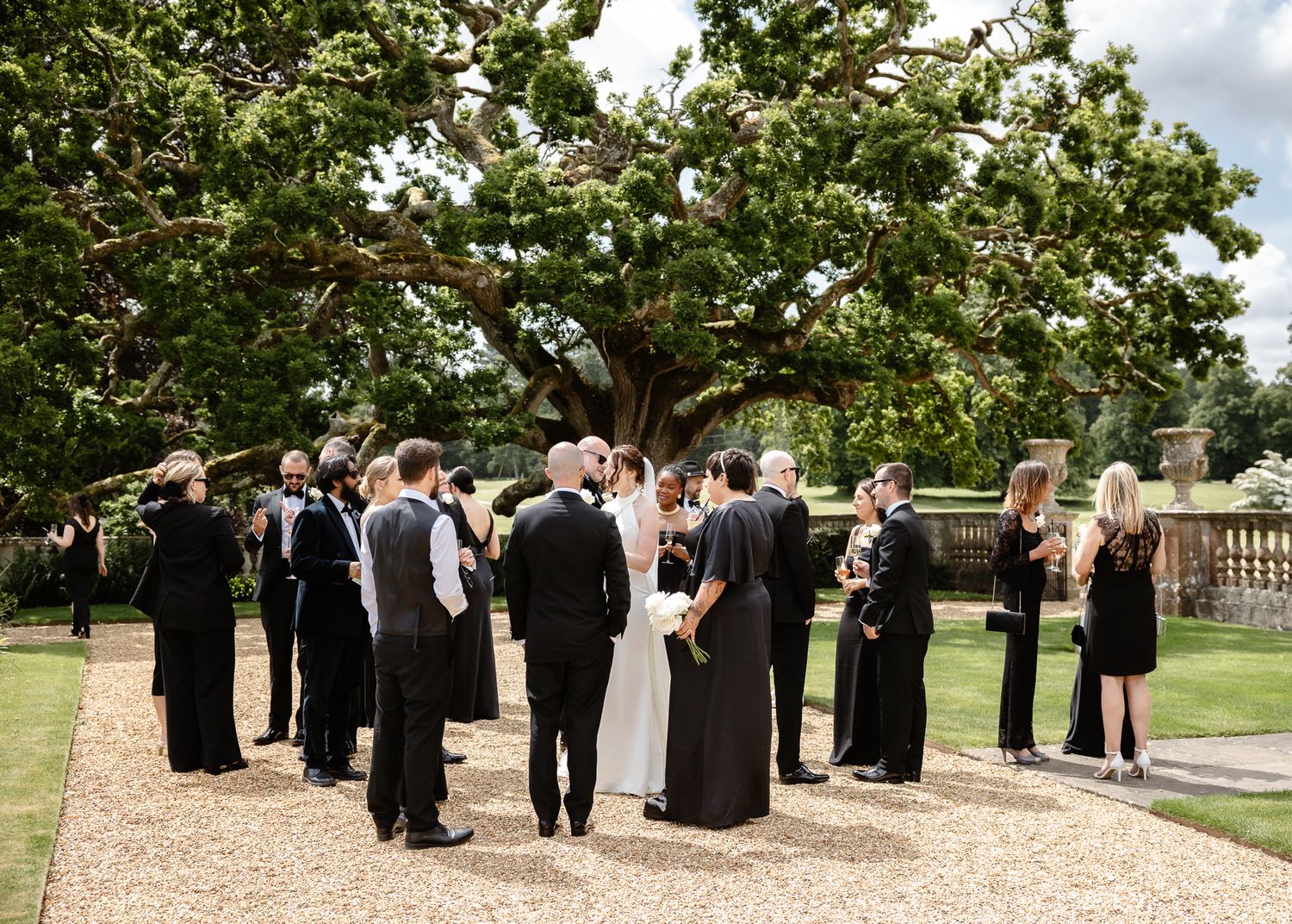 Wedding guests gathered on a gravel path surrounded by lush greenery at an outdoor venue.