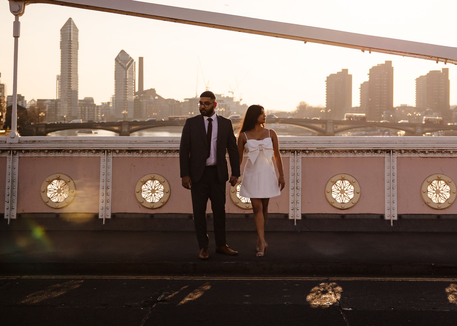 A couple stands silhouetted against a dramatic sunset skyline on a rooftop with round clock-like windows visible.