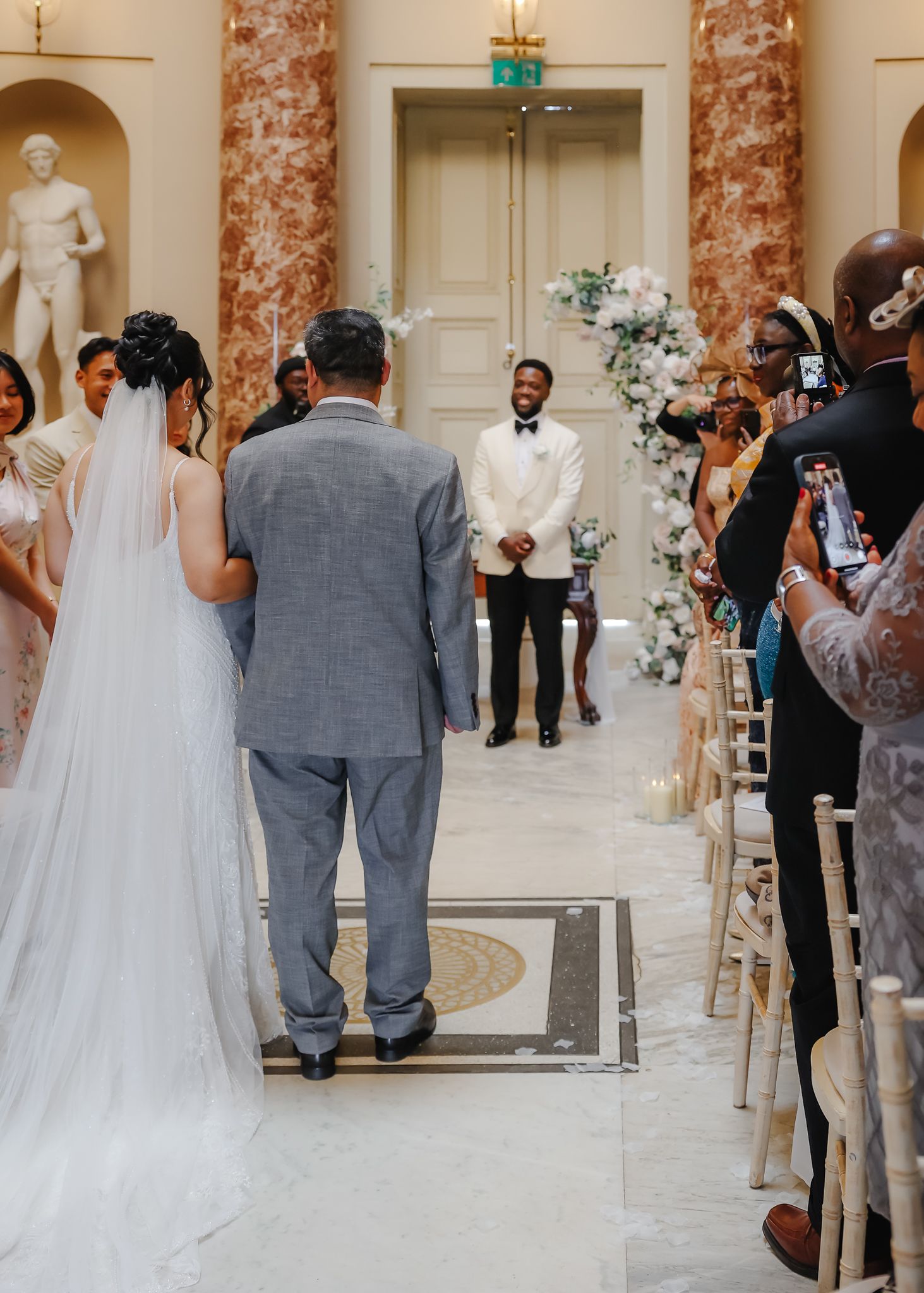 Elegant wedding ceremony in a grand marble-columned venue with guests watching the couple at the altar.