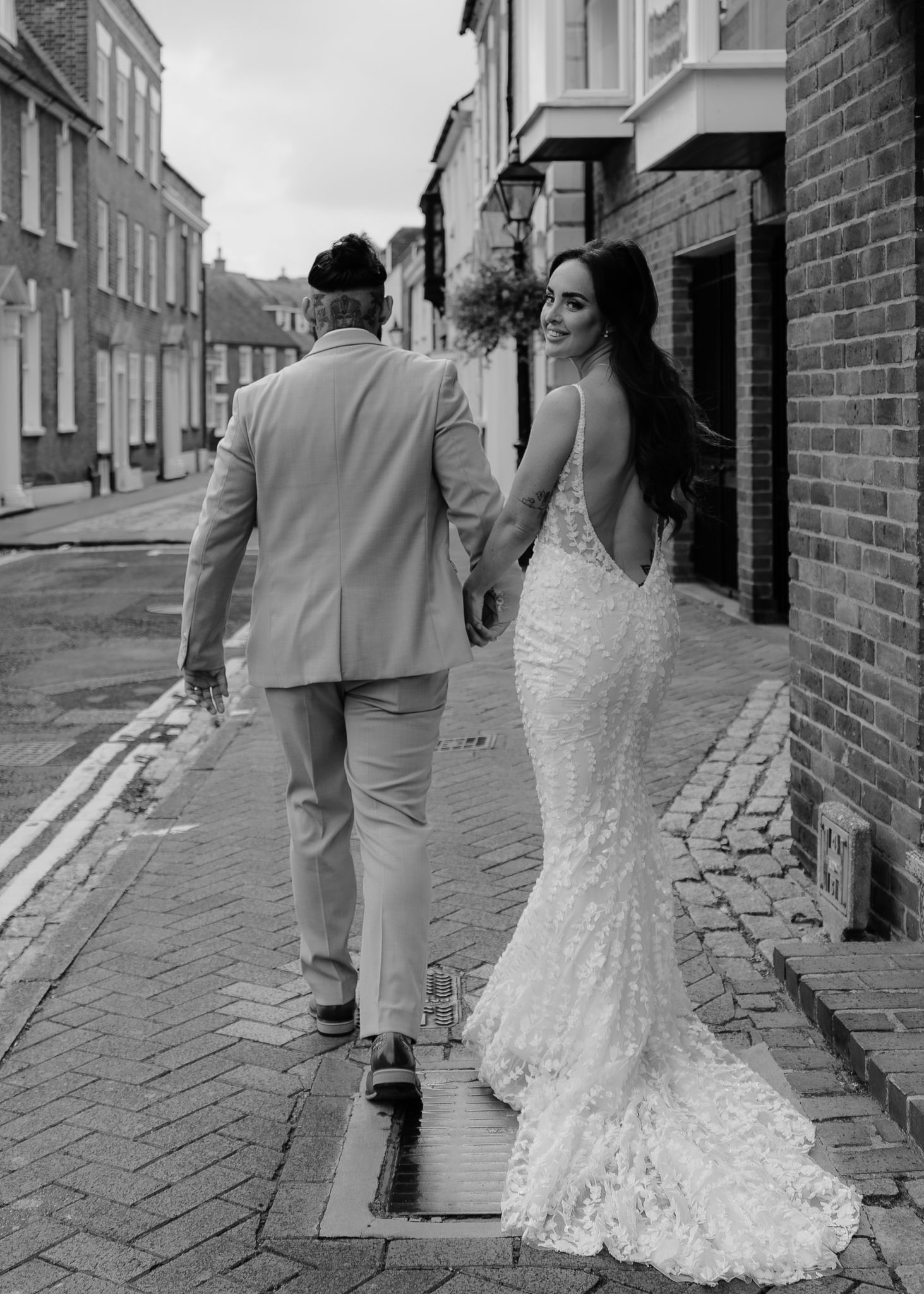 A couple in wedding attire walks down a cobblestone street with brick buildings, shown in multiple angles.