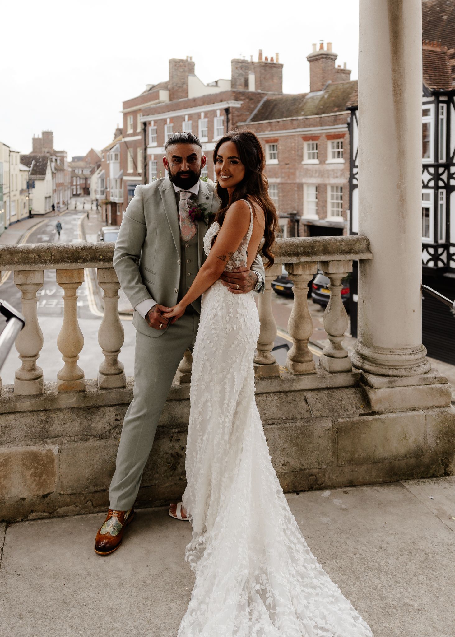 Elegant wedding couple poses on a classic stone balcony in formal attire during their special day.