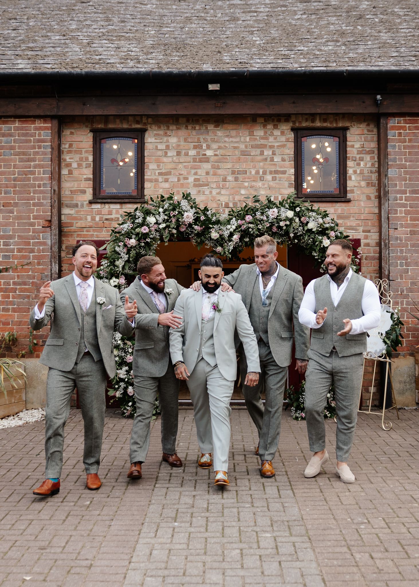 Wedding party in coordinated gray and white attire sitting together on brick pavement.
