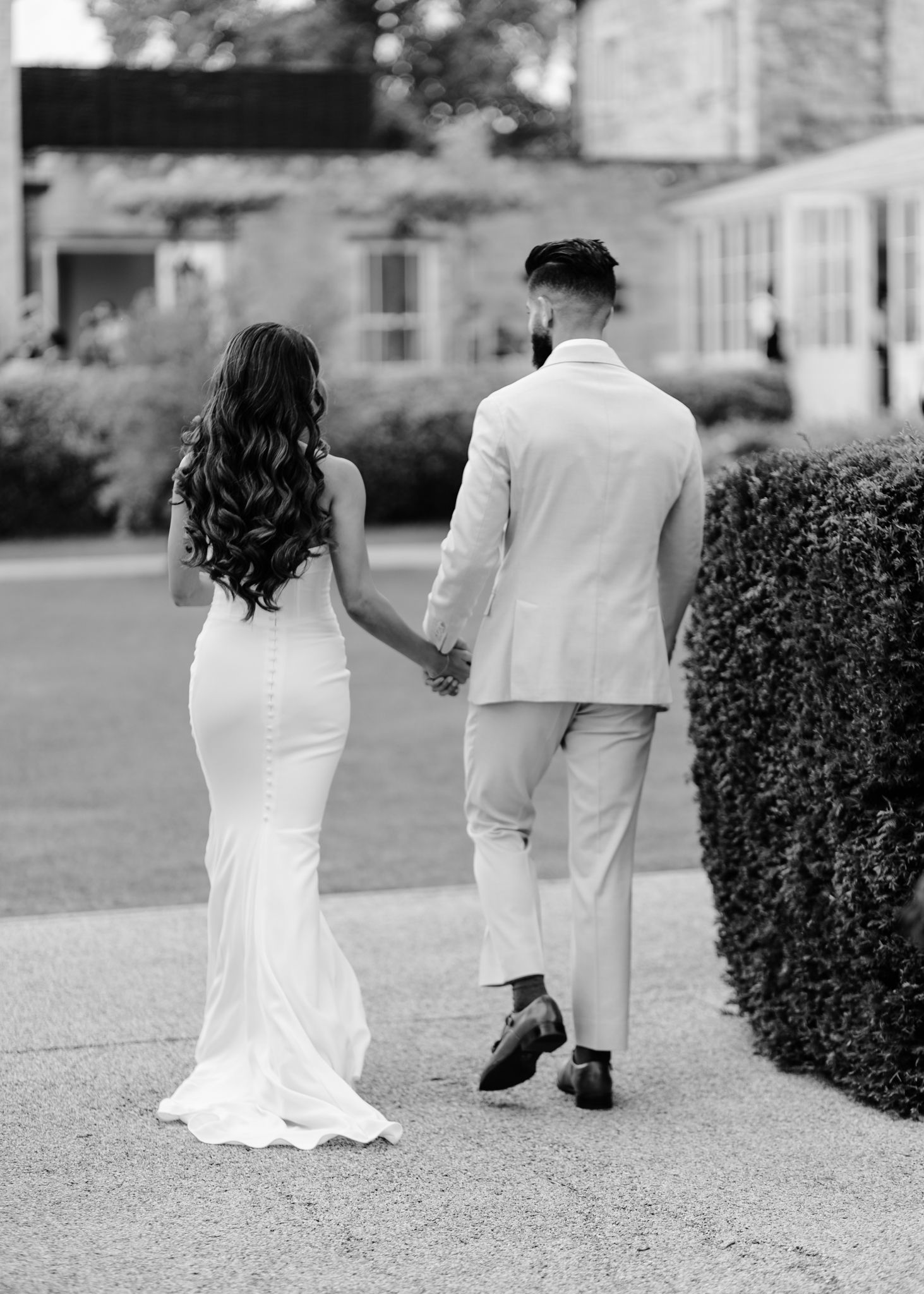 Black and white photo of a couple walking away on a path, showing their backs in formal wedding attire.