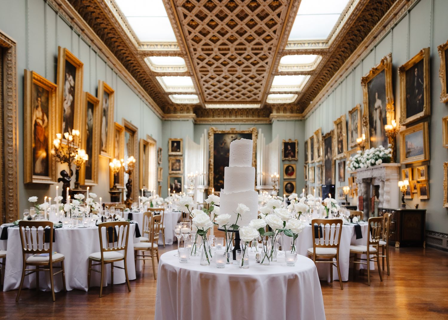 A luxurious wedding reception hall with detailed ceiling work and round tables set for an elegant celebration.