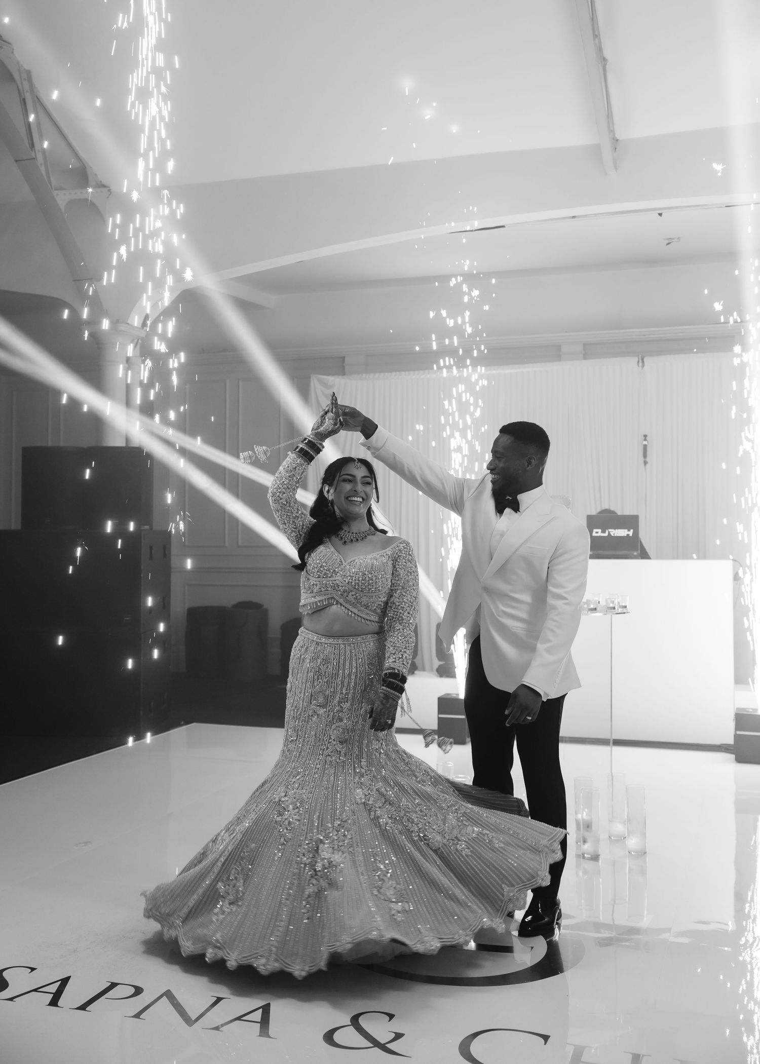 Couple shares first dance on illuminated floor with sparkling lights at Sapna wedding reception in black and white.
