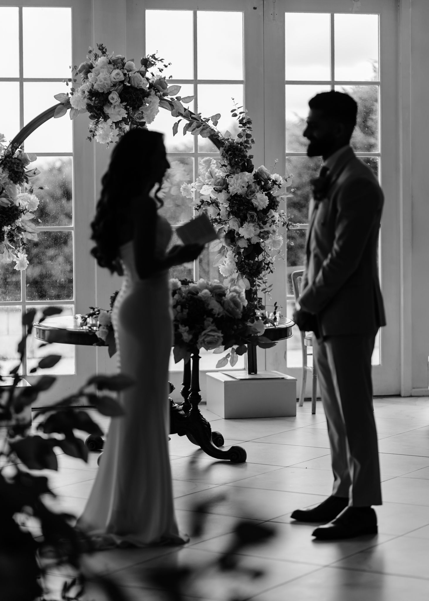 Black and white photo of a wedding ceremony with guests standing in a light-filled room.