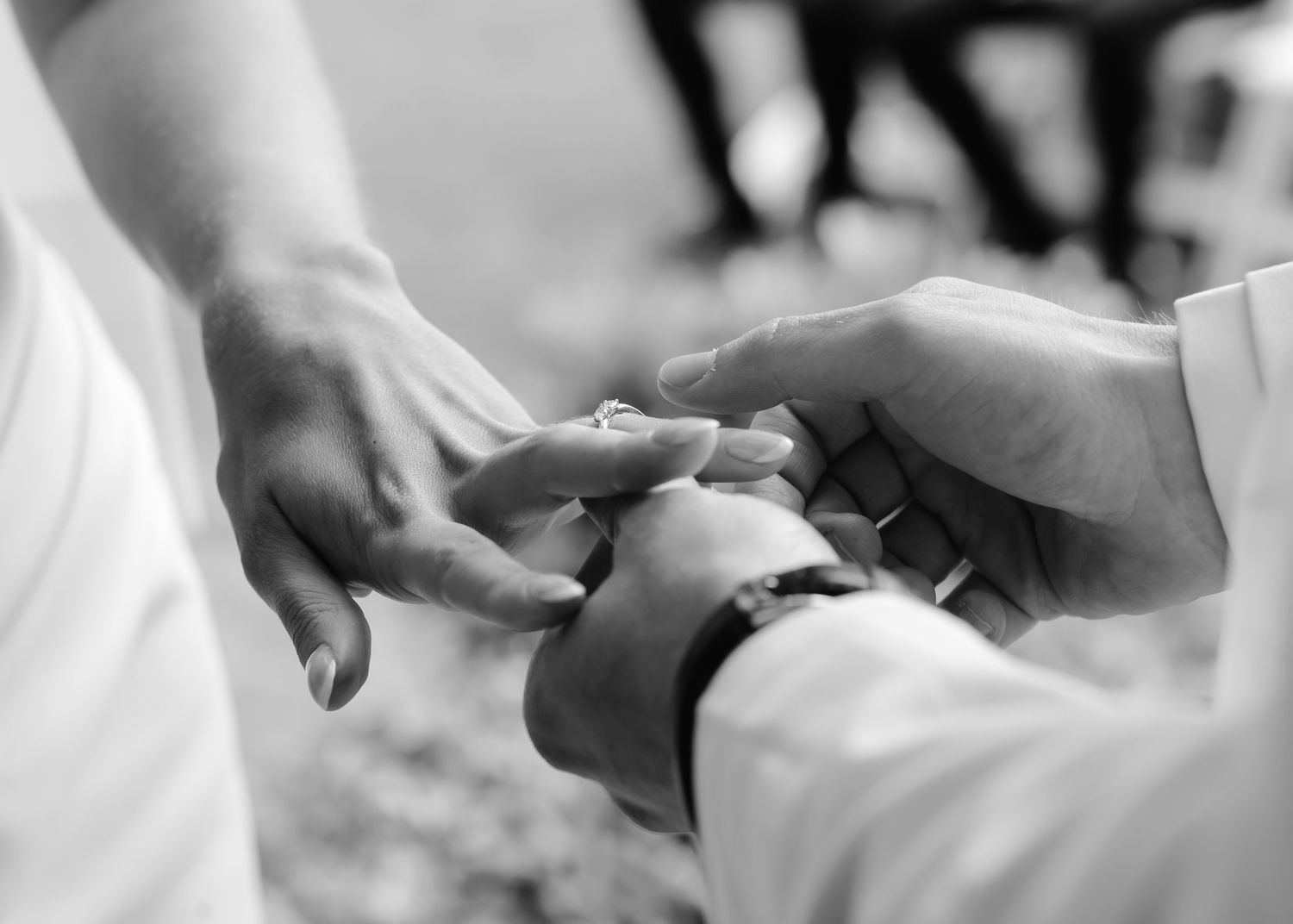 Close-up black and white photo of a groom placing a wedding ring on the brides finger.