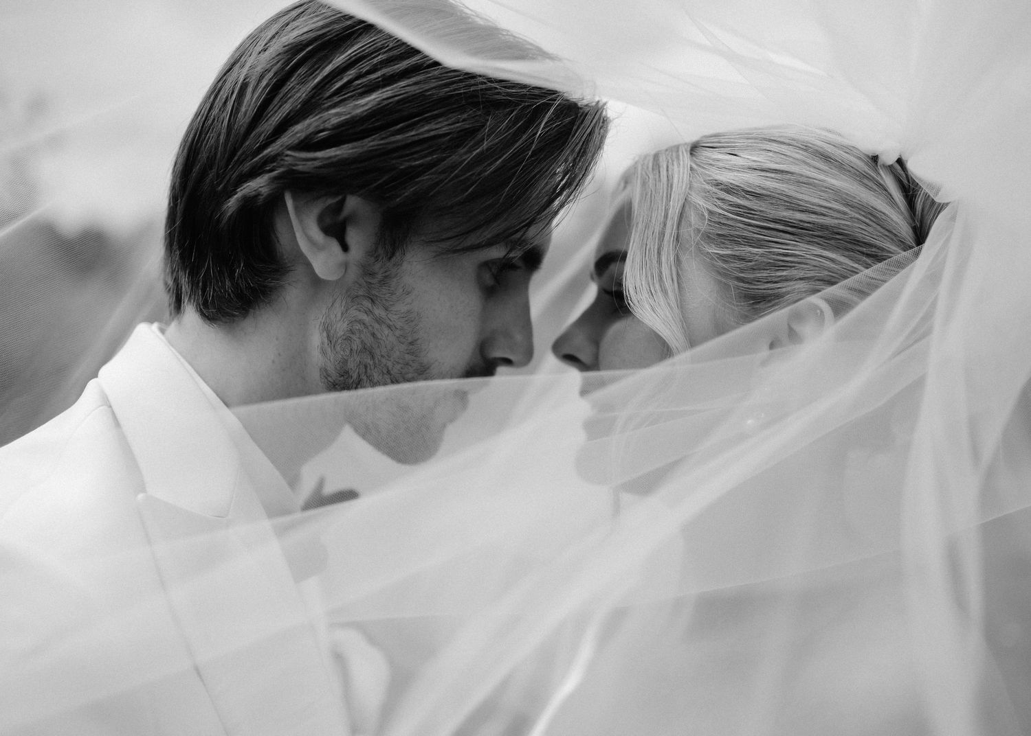 Black and white photo of bride and groom sharing intimate moment under wedding veil.