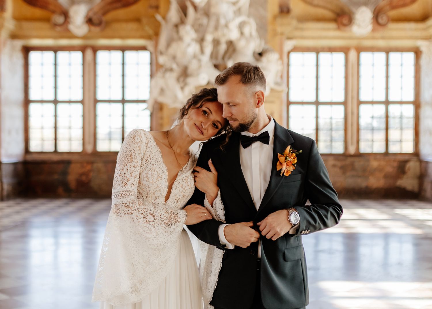 Elegant bride and groom sharing a tender moment in an ornate ballroom, wearing wedding dress and dark tuxedo.