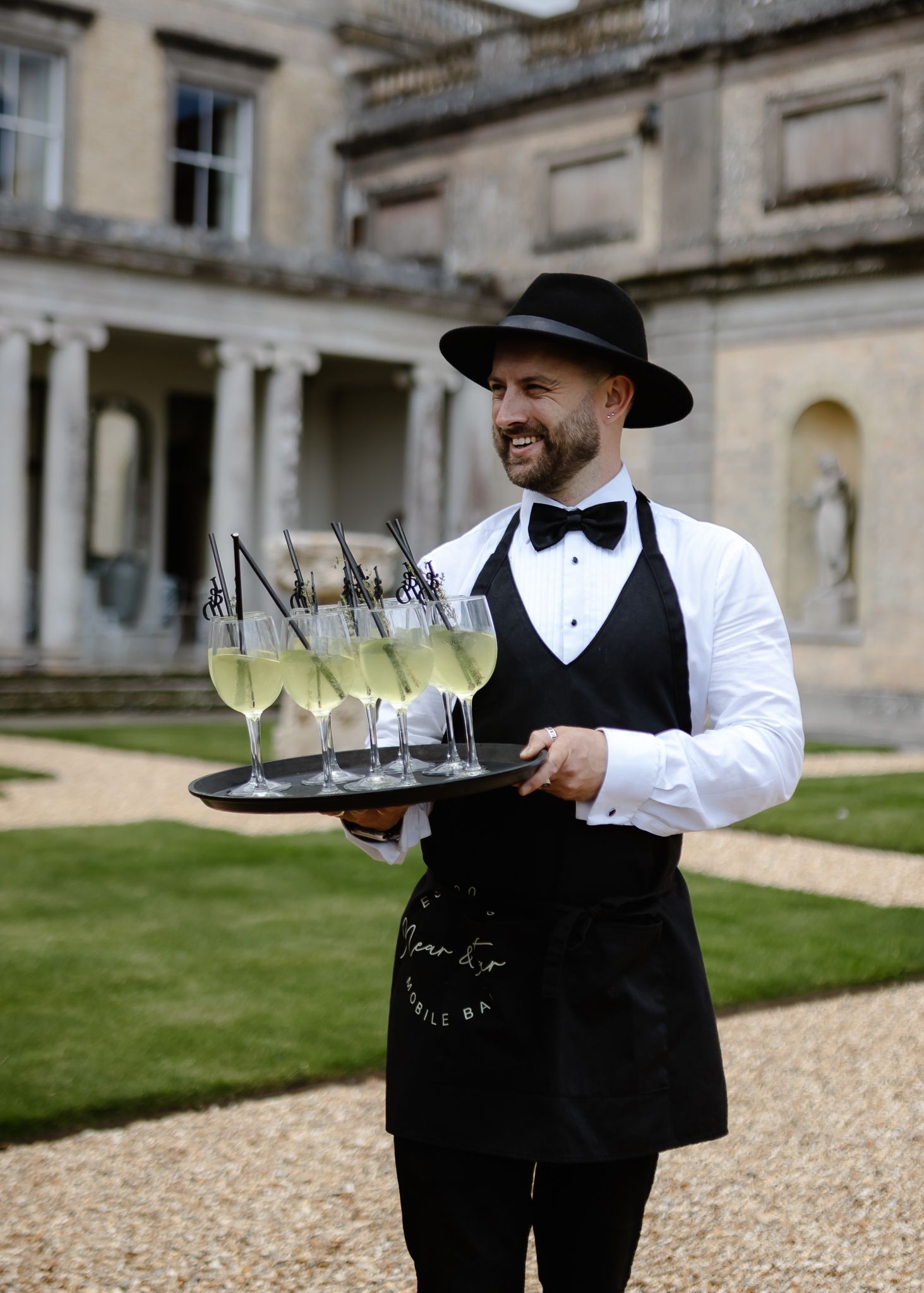 Waiters in formal black and white attire carrying trays of champagne glasses at an elegant event.