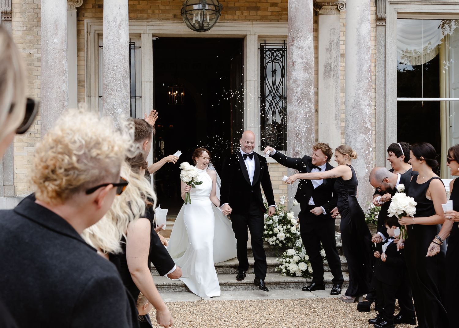 Wedding guests celebrate and take photos outside a grand historic building entrance.