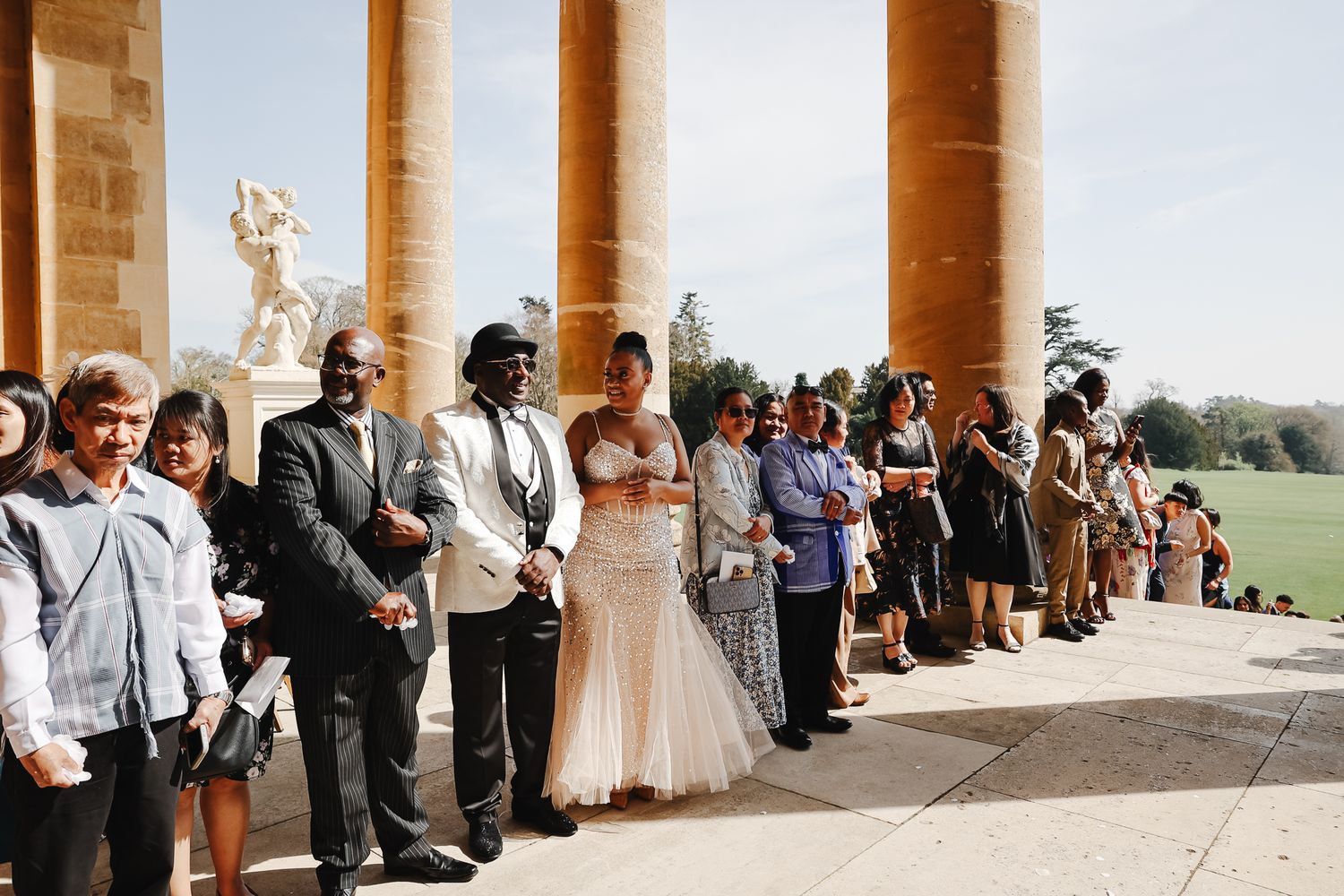 Wedding guests gathered under elegant stone columns at an outdoor venue with scenic countryside views.