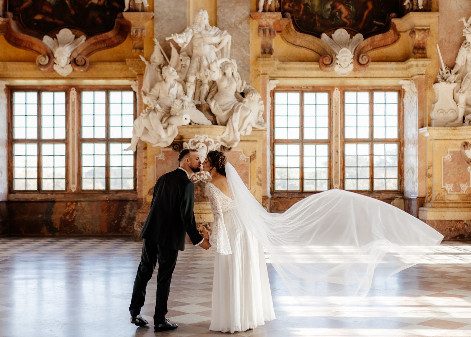 A couple dances together in an ornate baroque ballroom with elegant marble columns and large windows.