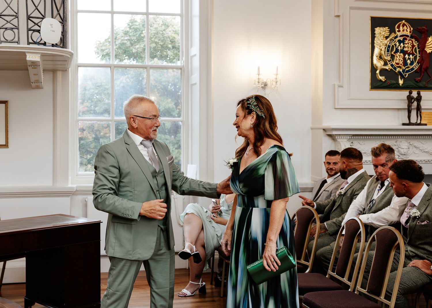 Wedding guests gather in an elegant white room with large windows and hardwood floors during a ceremony.