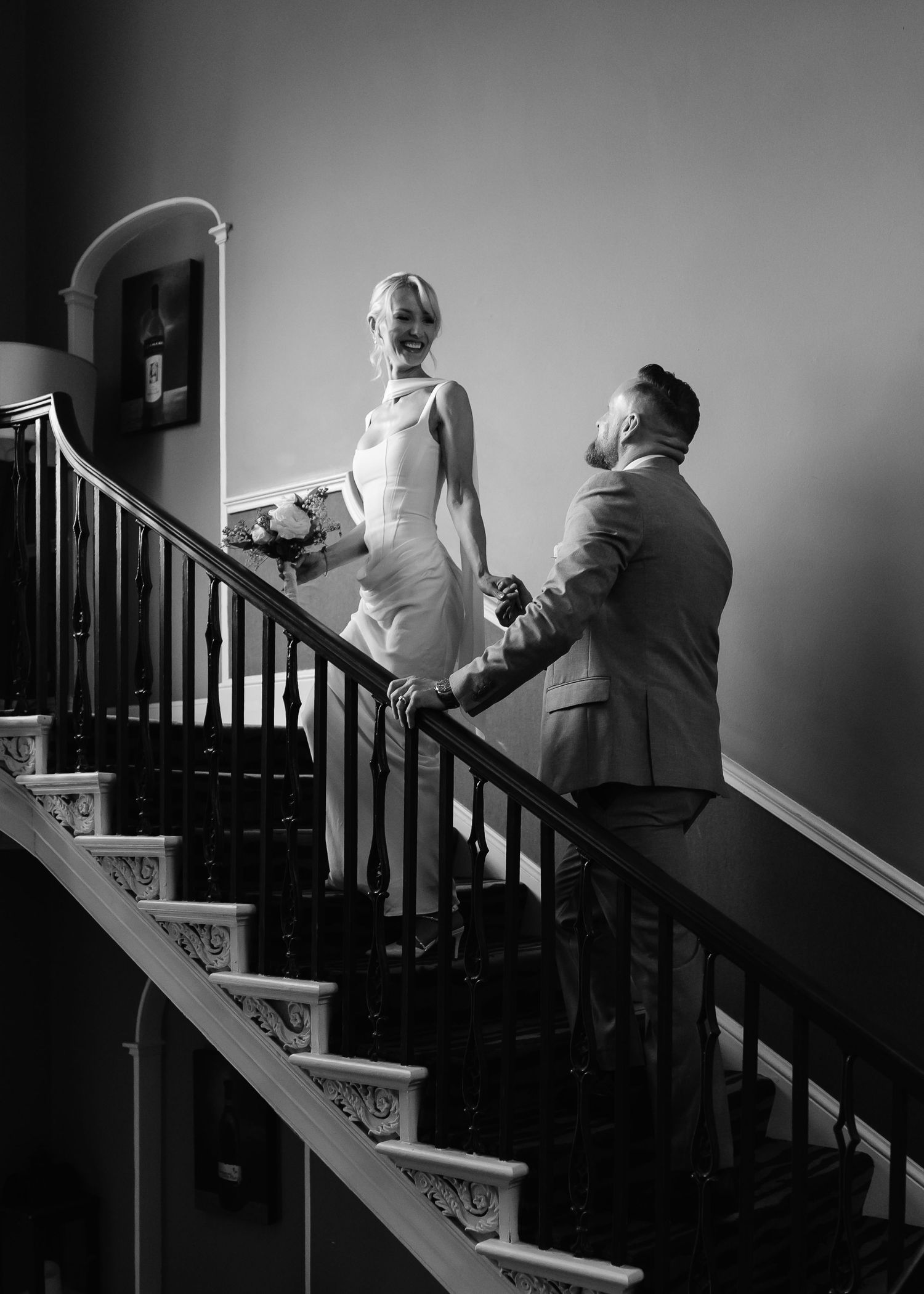 Black and white wedding photo of bride and groom holding hands on elegant staircase.