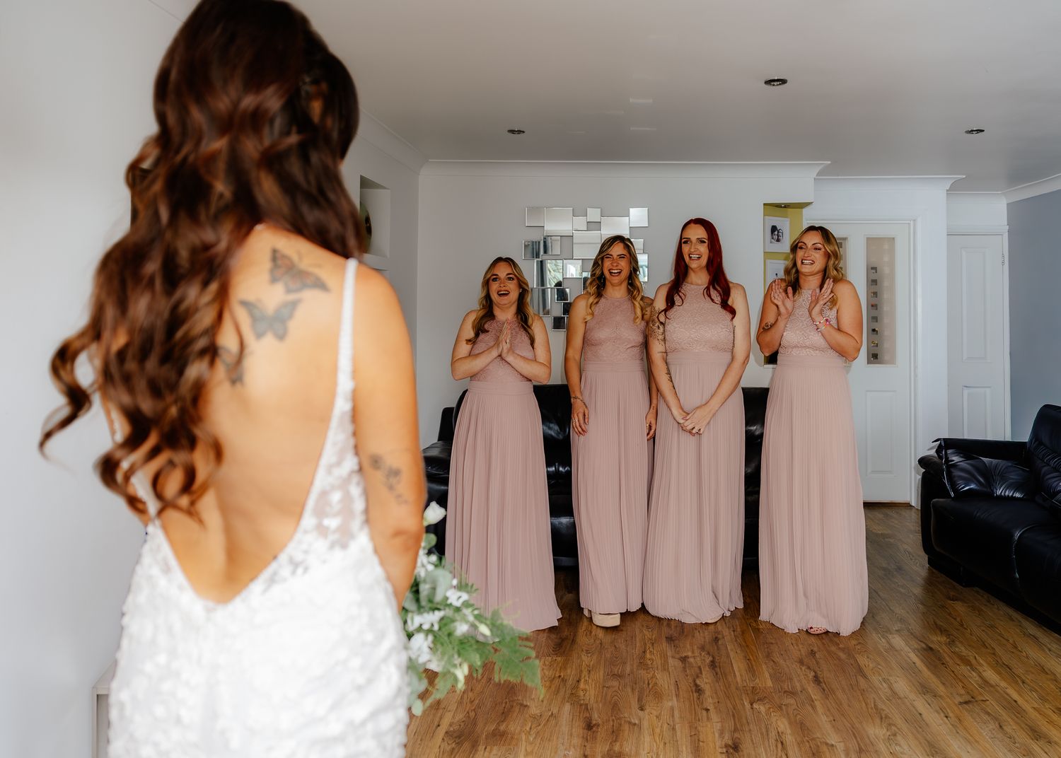 Bridesmaids in blush pink dresses stand together while getting ready for a wedding celebration.