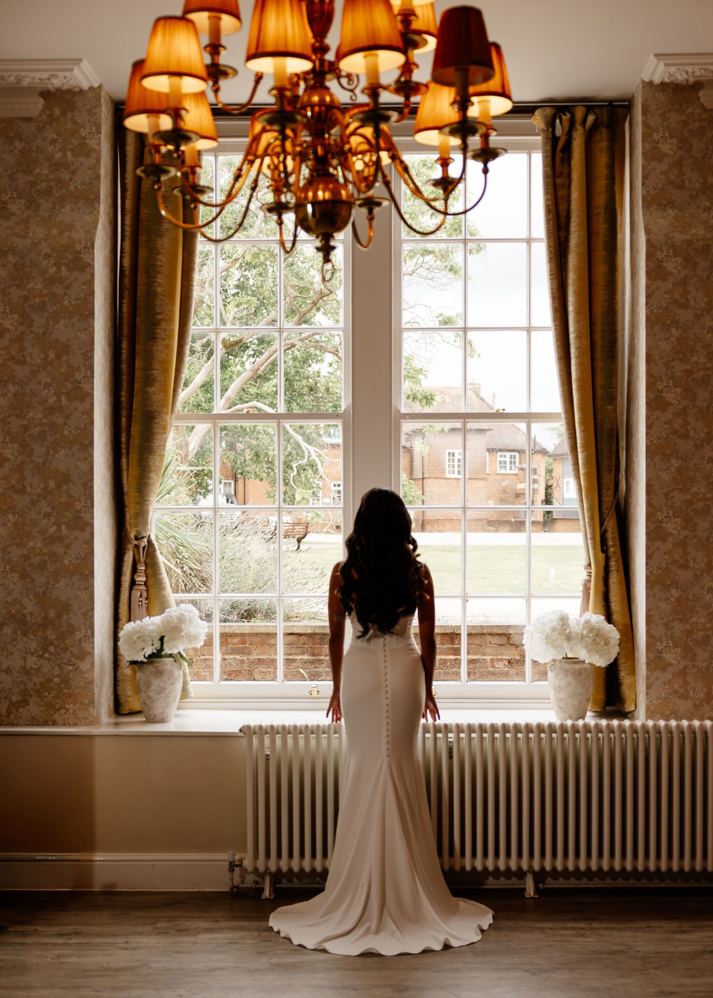 Elegant room interior with chandelier, floral wallpaper, and large windows with golden curtains.