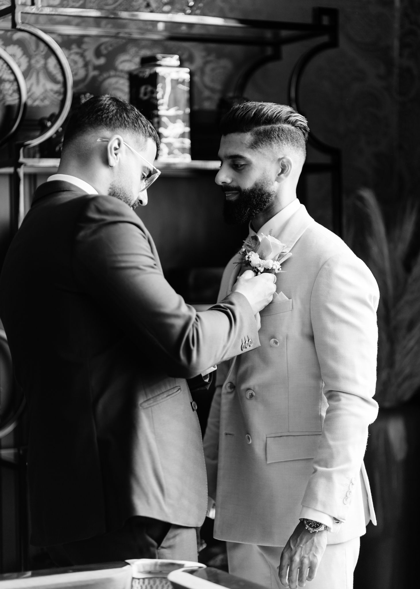 Two men in formal attire share a light-hearted moment together in a dimly lit setting.