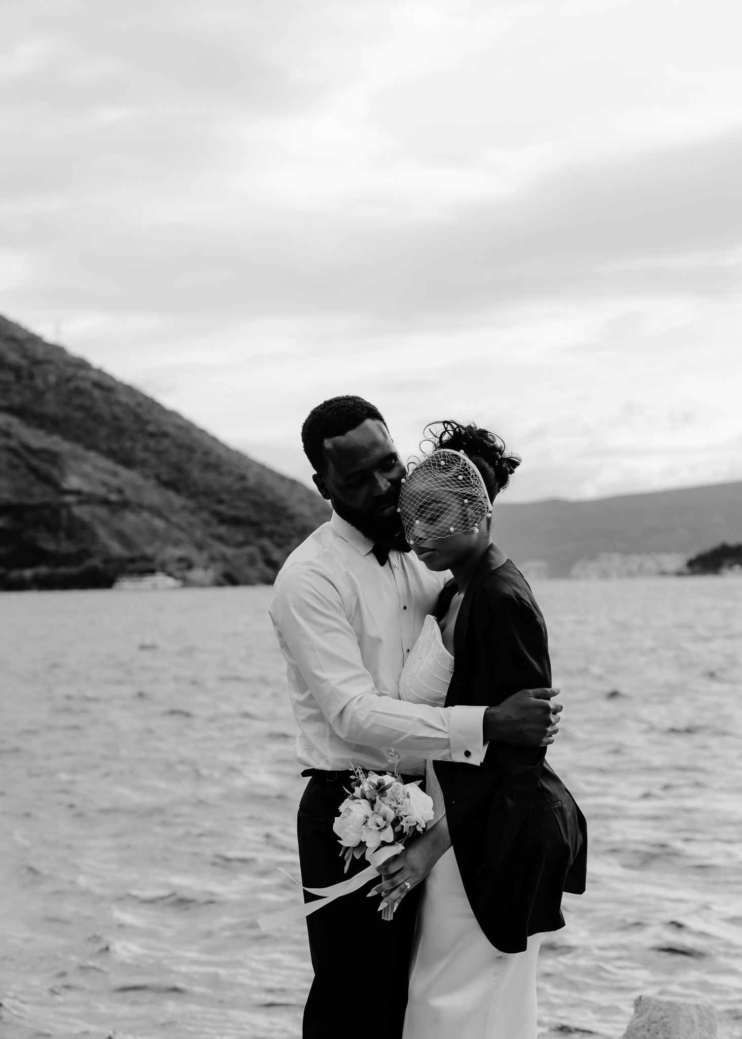 A romantic couple embraces by the ocean in a series of black and white photos showing tender moments against a coastal backdrop.