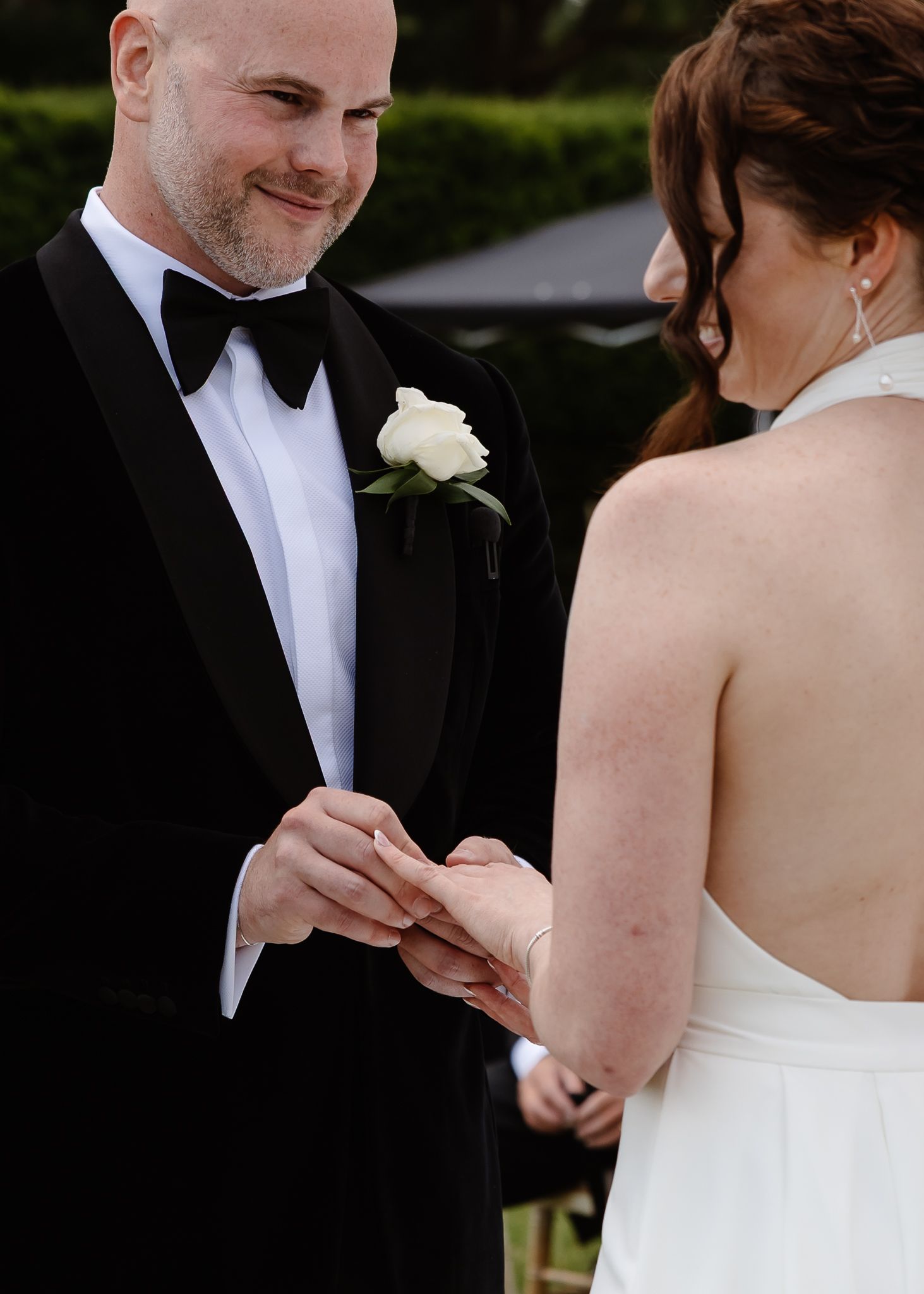 Close-up shots of hands exchanging rings during an outdoor wedding ceremony.