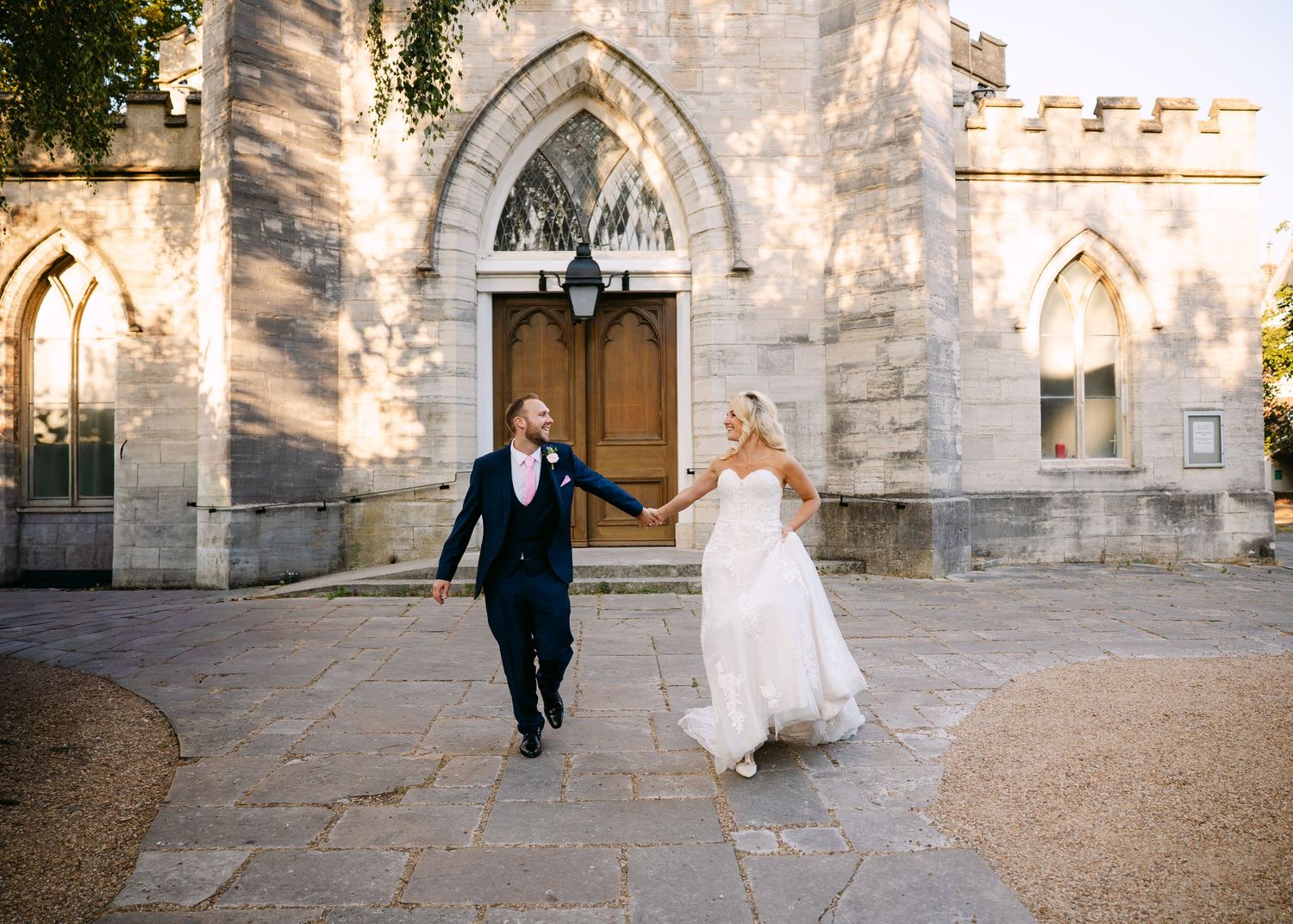 Bride and groom holding hands walking outside a historic stone church on their wedding day.