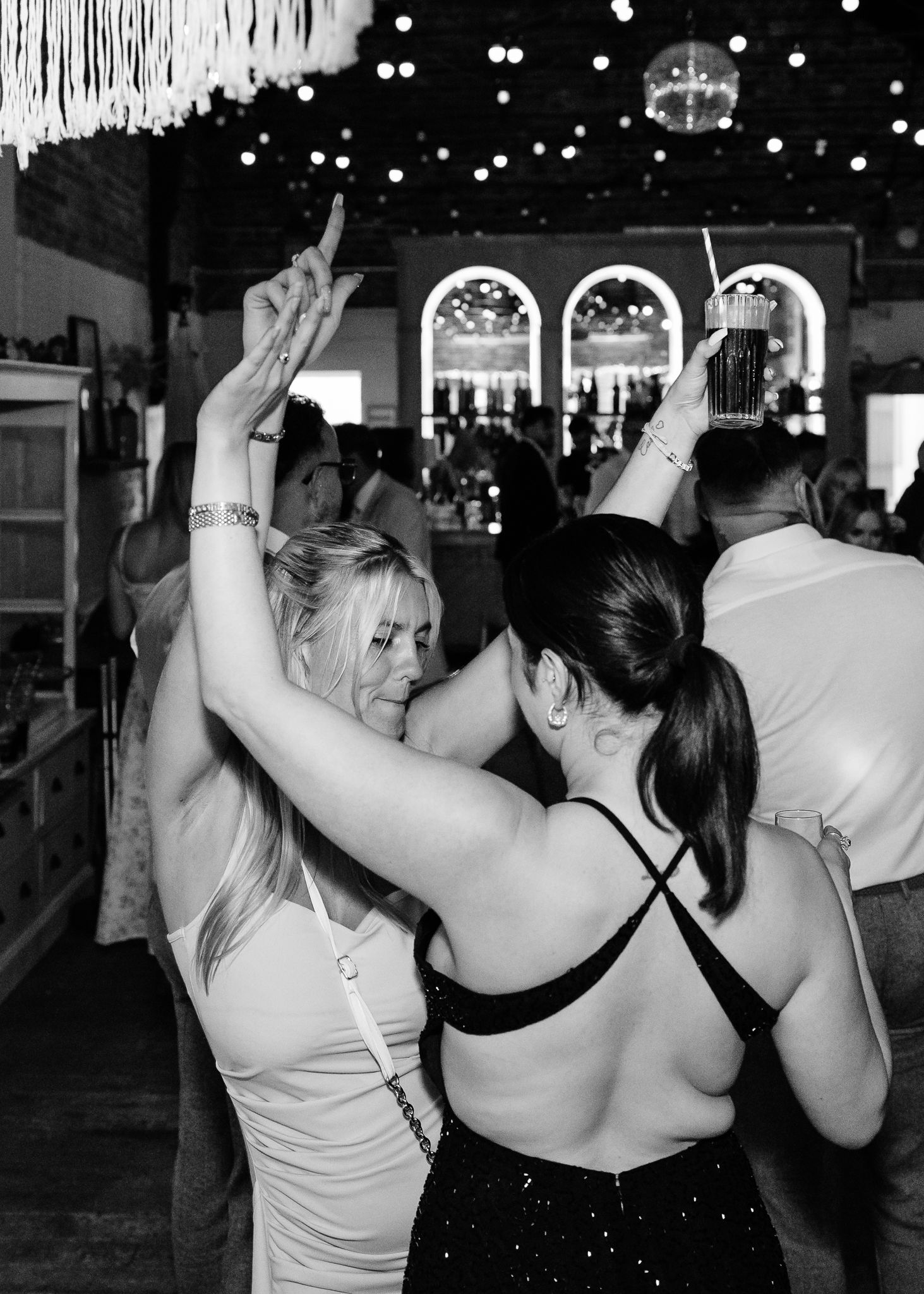 Party guests dancing under string lights and disco ball at indoor reception venue.