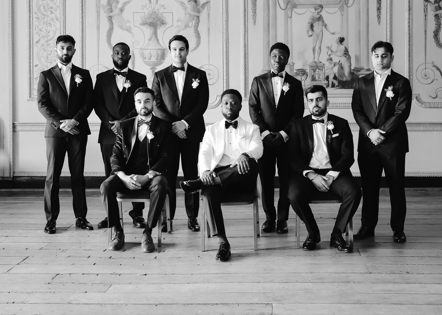 Black and white photo of groomsmen sitting on floor showing off their colorful patterned socks at a formal wedding.