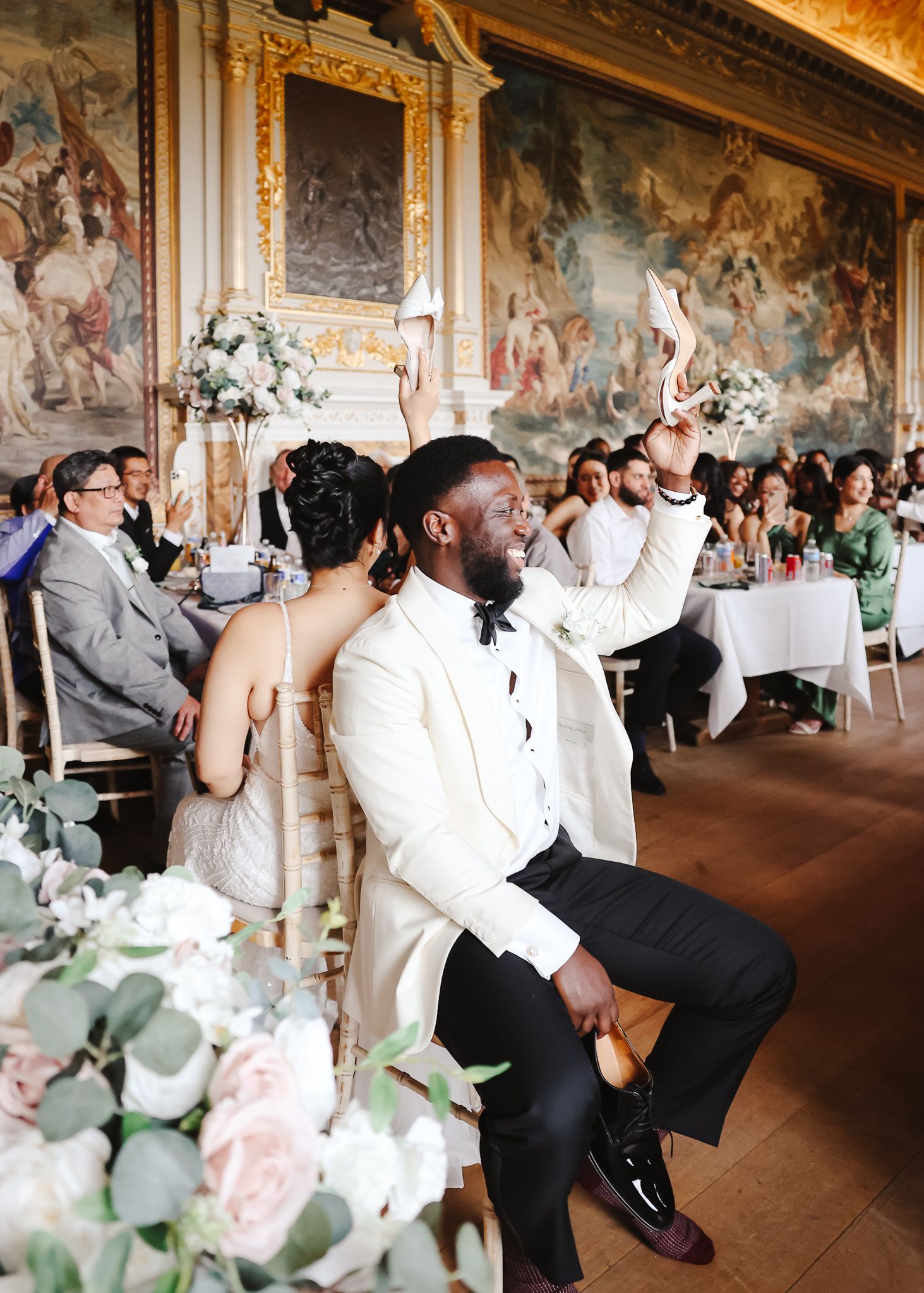 Wedding couple performs choreographed dance moves in an ornate ballroom with frescoed walls and guests watching.