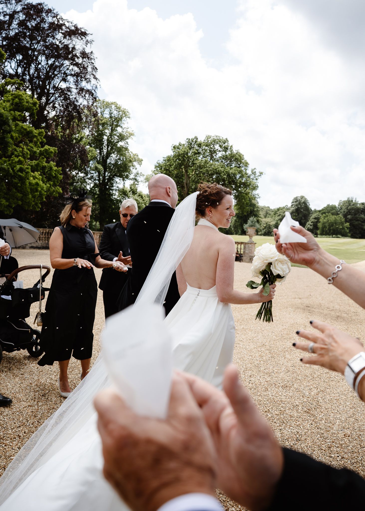 Wedding guests throw confetti at the newlyweds during an outdoor celebration.