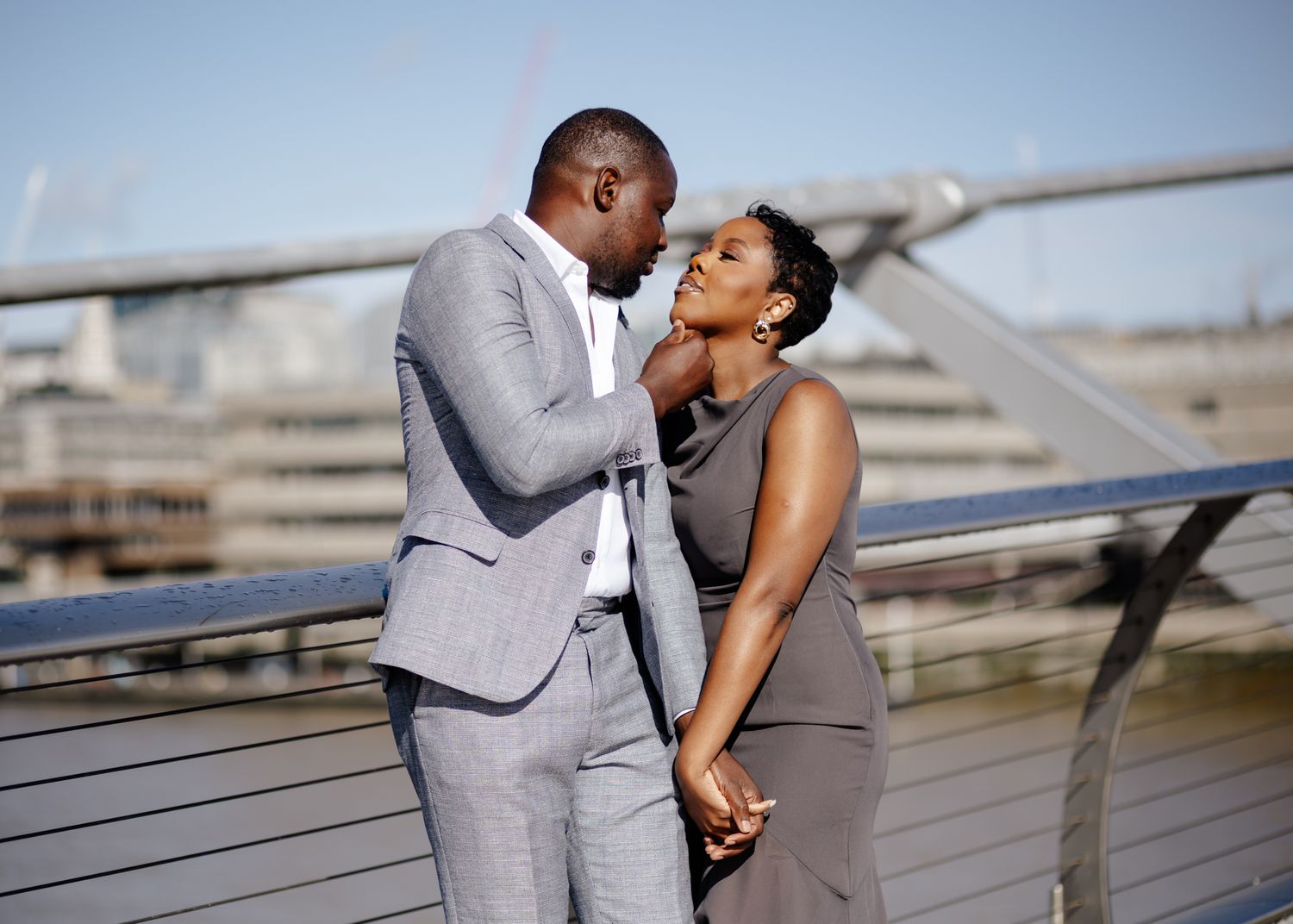 A romantic couple in formal attire shares an intimate moment along a waterfront railing.