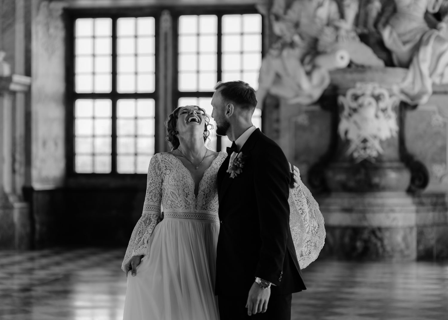 A romantic wedding couple dances together in an ornate ballroom with elegant frescoed walls and windows.