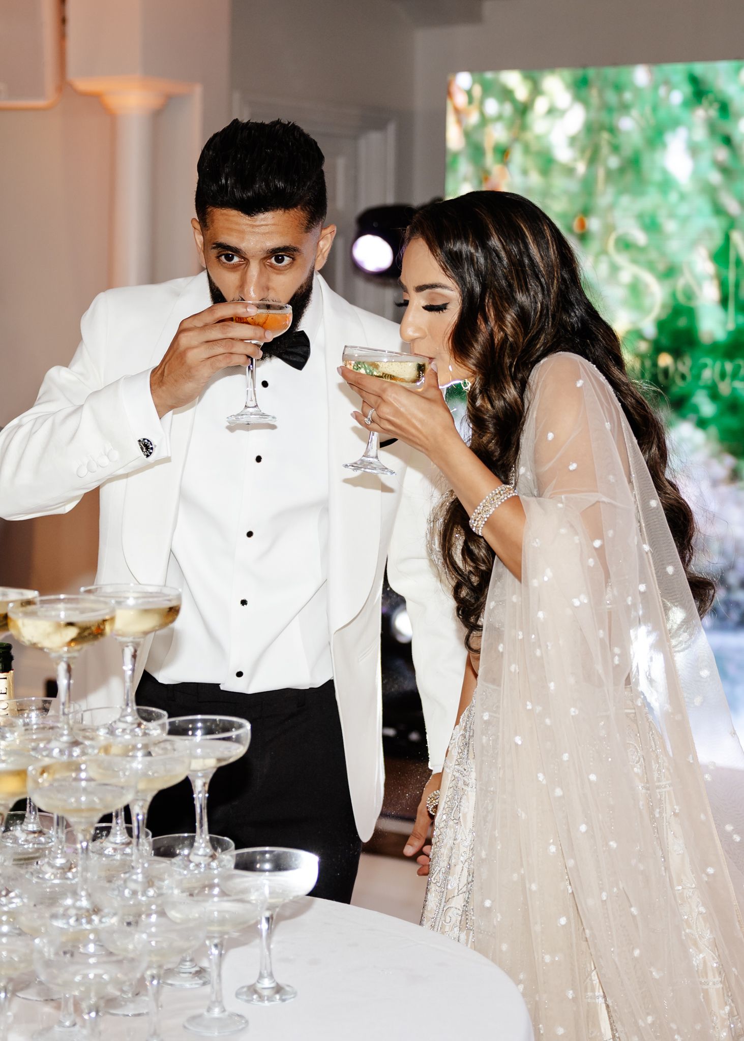 A couple in formal wedding attire sips champagne together at their reception celebration.